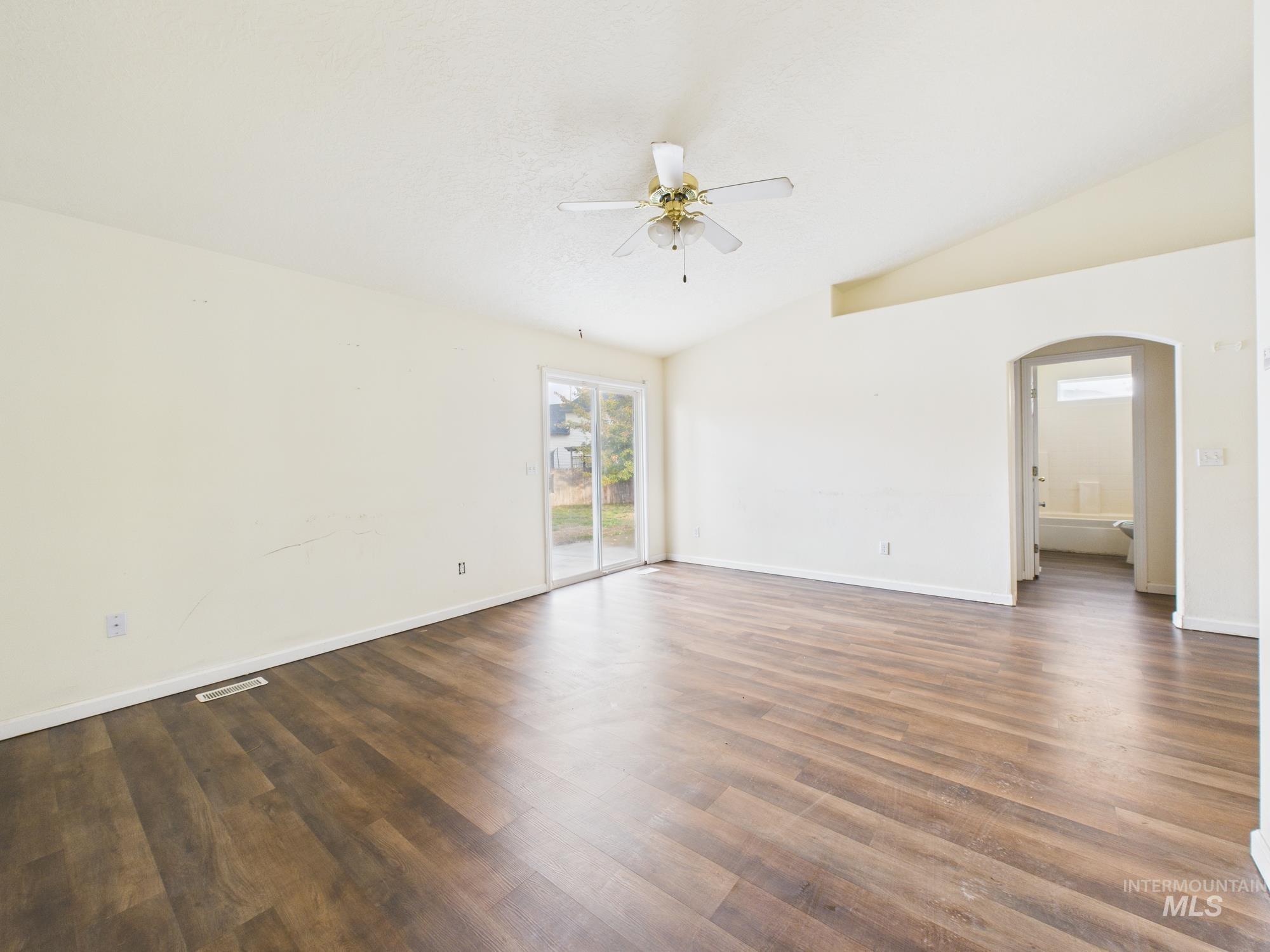 Empty room featuring lofted ceiling, dark wood-style floors, a ceiling fan, and arched walkways