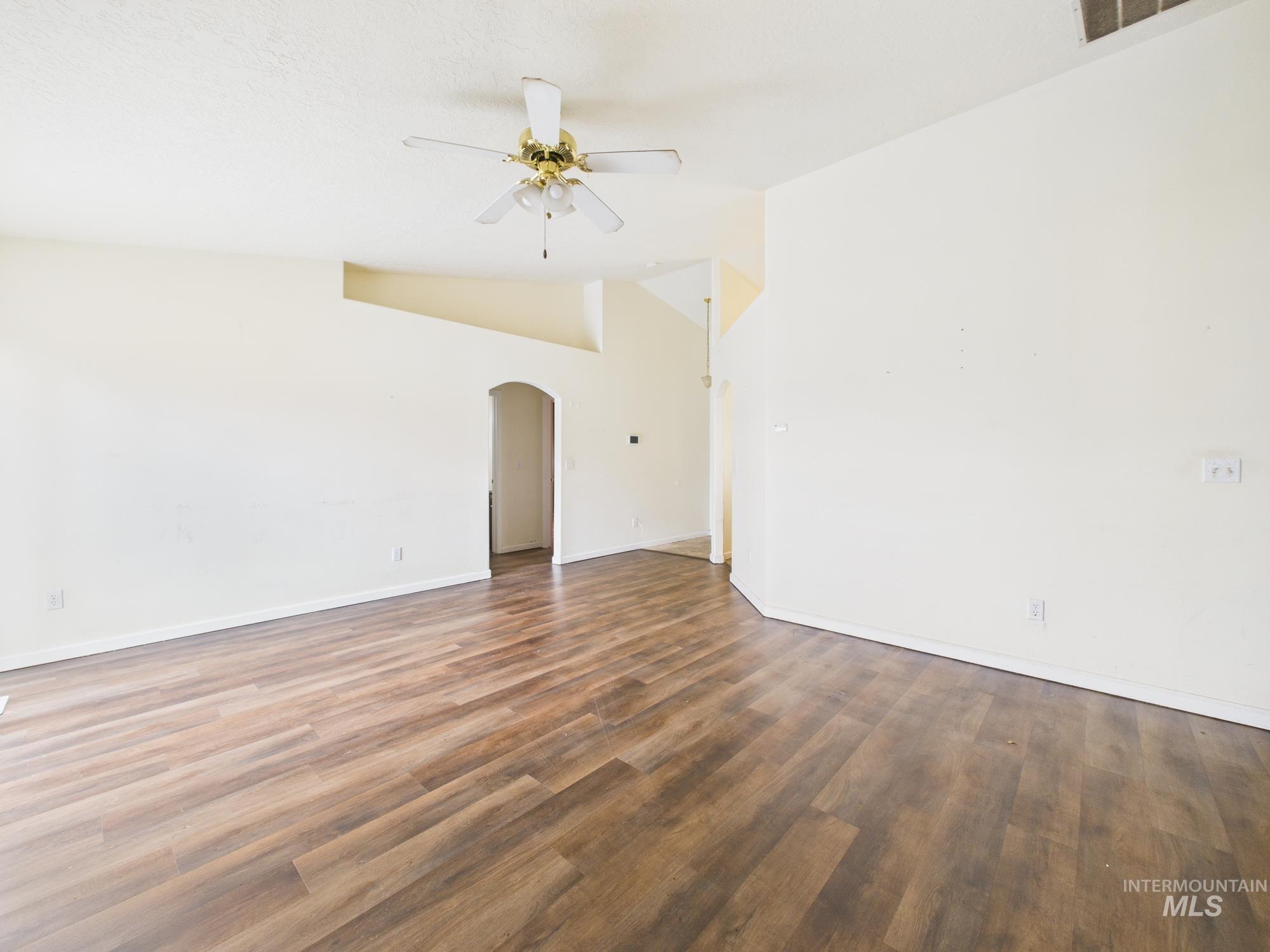 Empty room featuring arched walkways, vaulted ceiling, dark wood-style flooring, and a ceiling fan