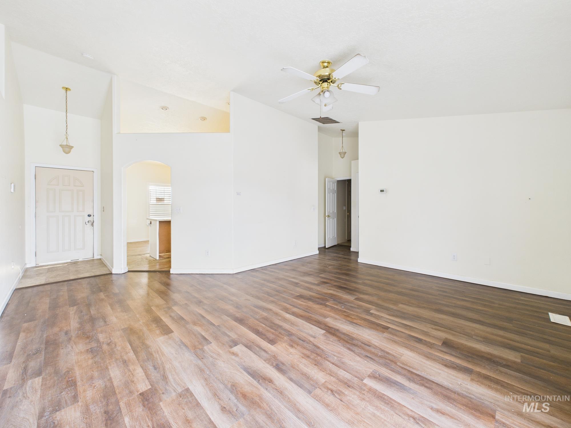 Unfurnished living room with wood finished floors, arched walkways, high vaulted ceiling, and a ceiling fan