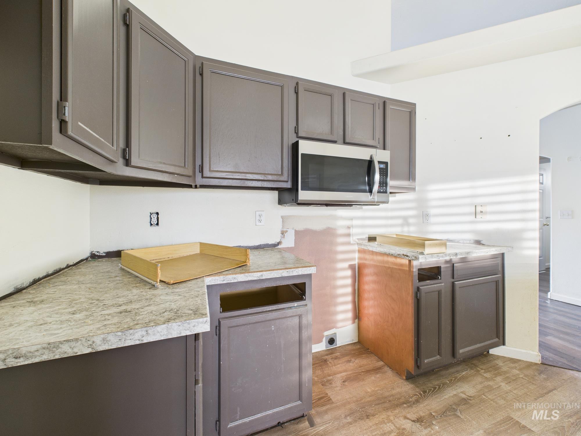 Kitchen featuring light wood-type flooring, light countertops, stainless steel microwave, and arched walkways