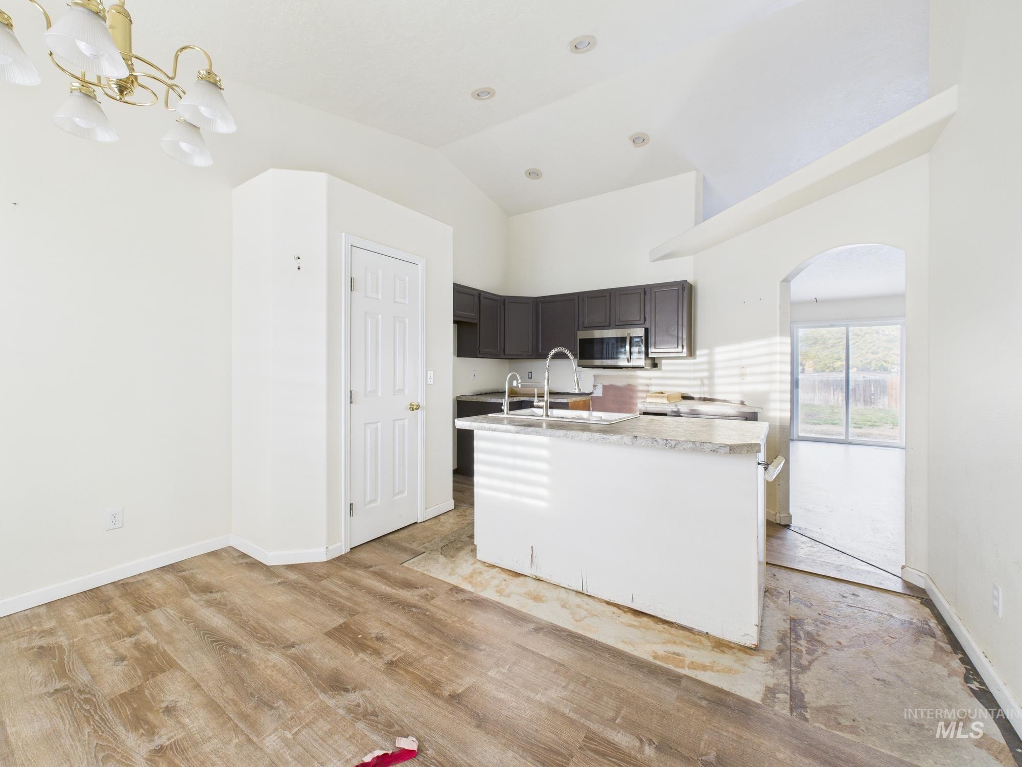 Kitchen with light countertops, a center island with sink, light wood-style flooring, stainless steel microwave, and high vaulted ceiling