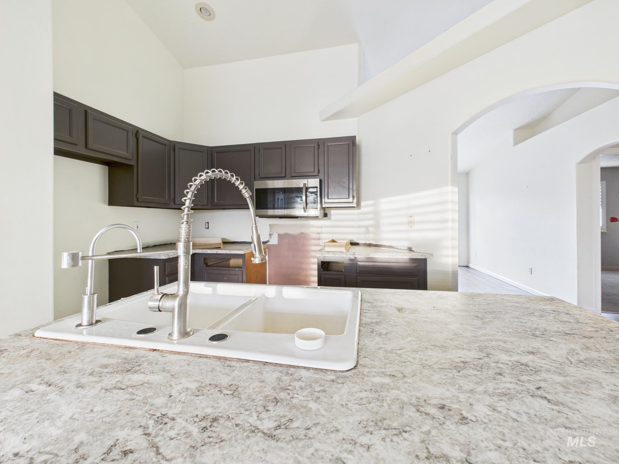 Kitchen with light countertops, stainless steel microwave, arched walkways, and dark brown cabinetry