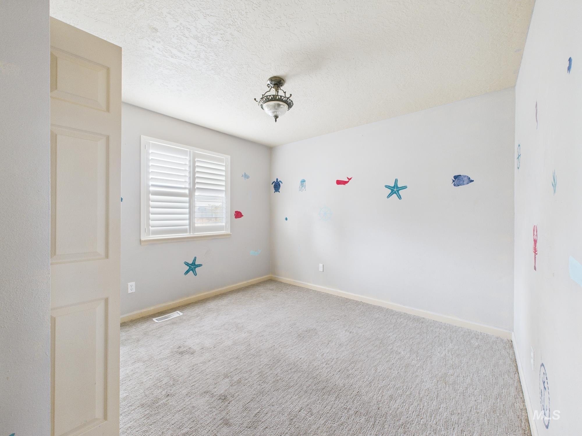 Carpeted spare room featuring a textured ceiling and baseboards