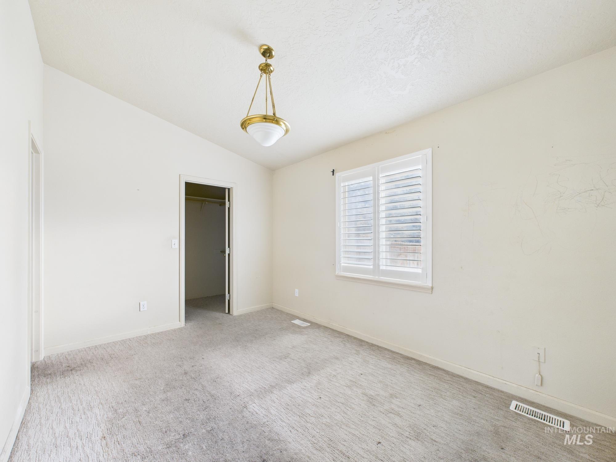 Unfurnished bedroom featuring a walk in closet, carpet, and lofted ceiling