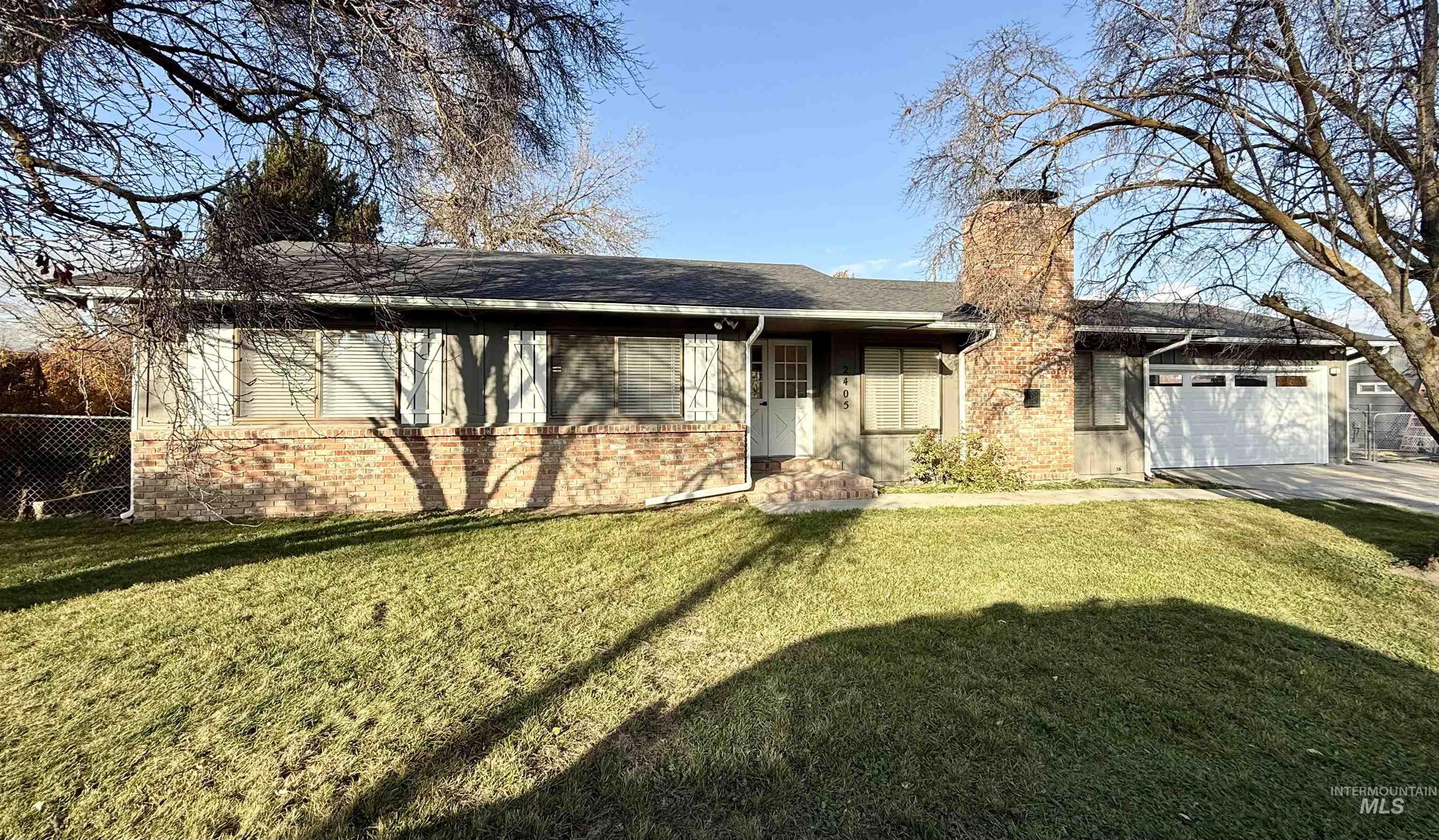 Ranch-style house with a chimney, an attached garage, brick siding, and roof with shingles