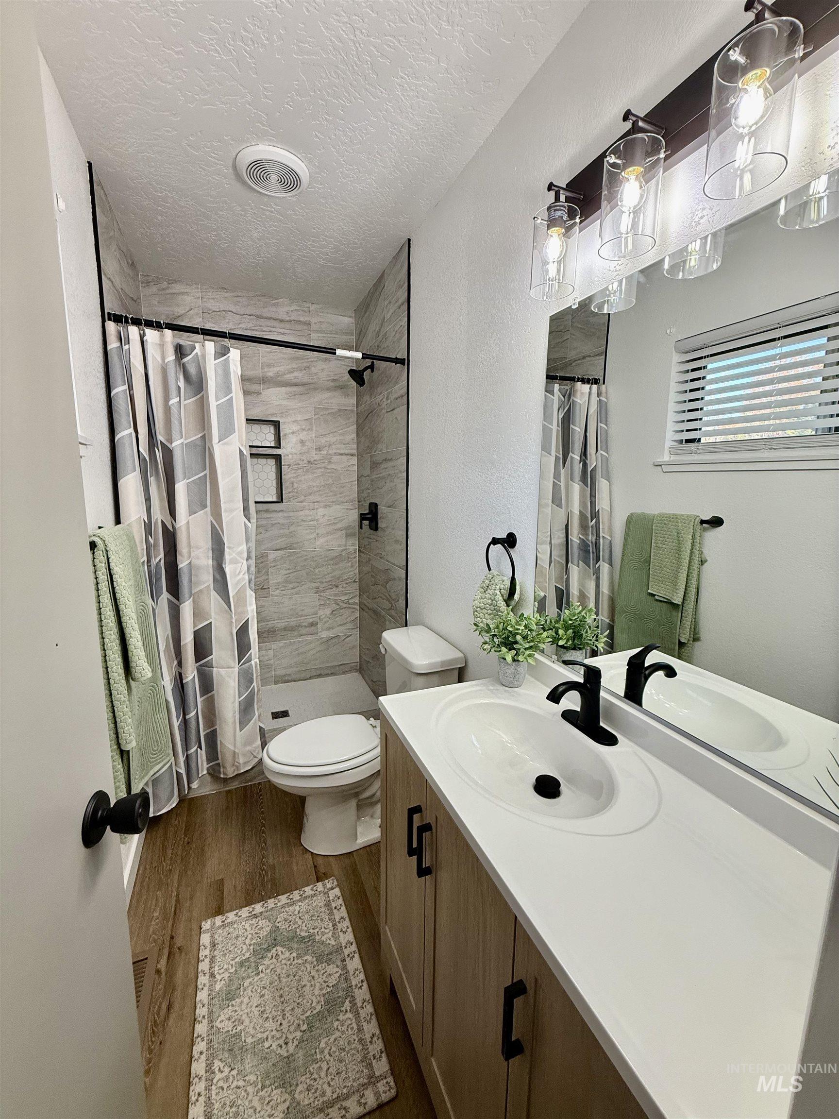 Full bathroom featuring vanity, a tile shower, dark wood-type flooring, a textured ceiling, and a textured wall
