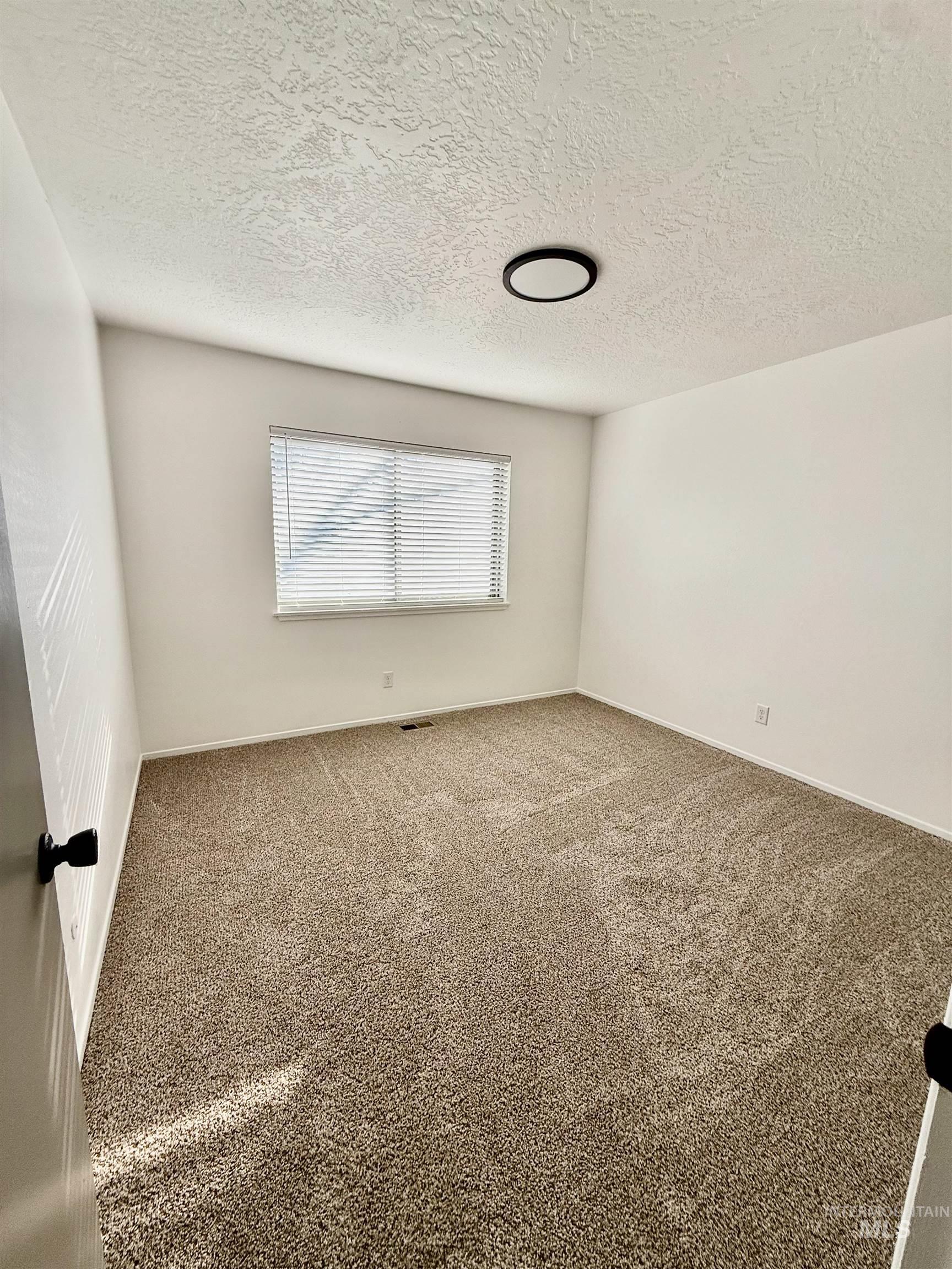 Carpeted spare room with a textured ceiling and baseboards