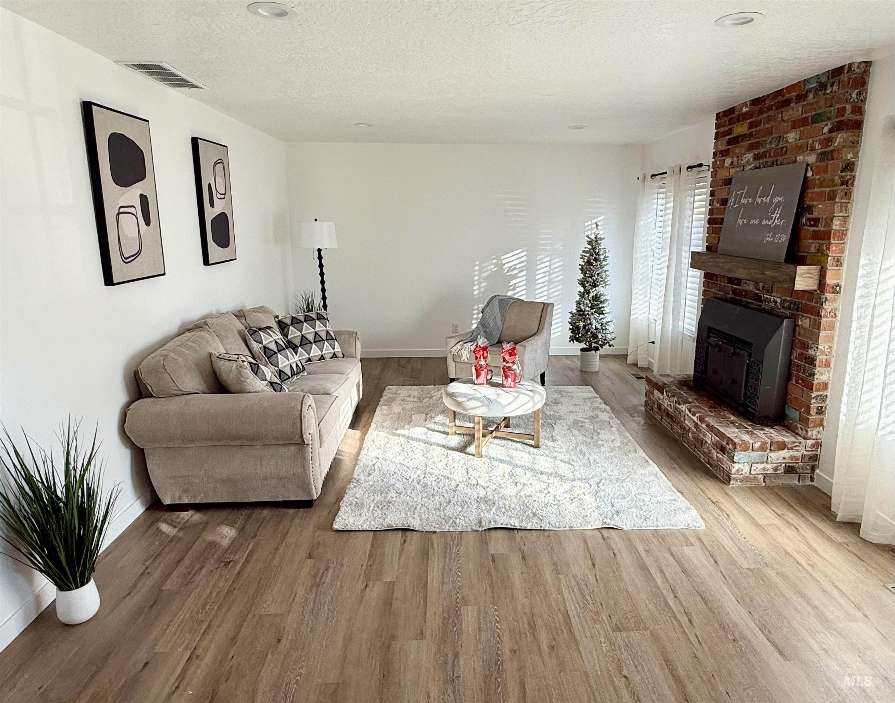 Living room featuring a textured ceiling, wood finished floors, and a brick fireplace