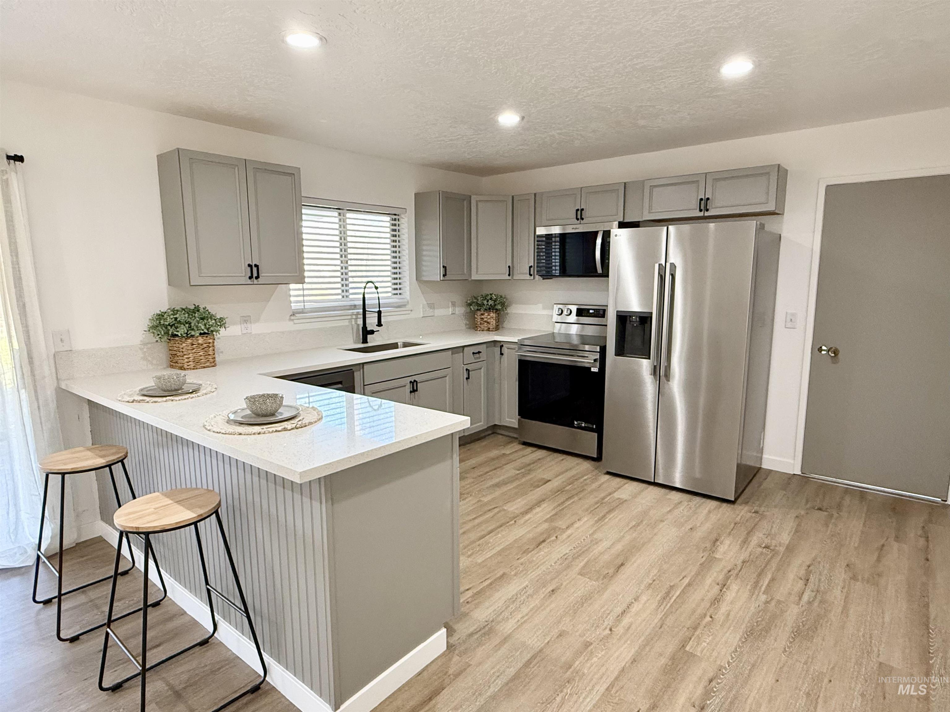 Kitchen featuring gray cabinetry, stainless steel appliances, a breakfast bar, a peninsula, and recessed lighting