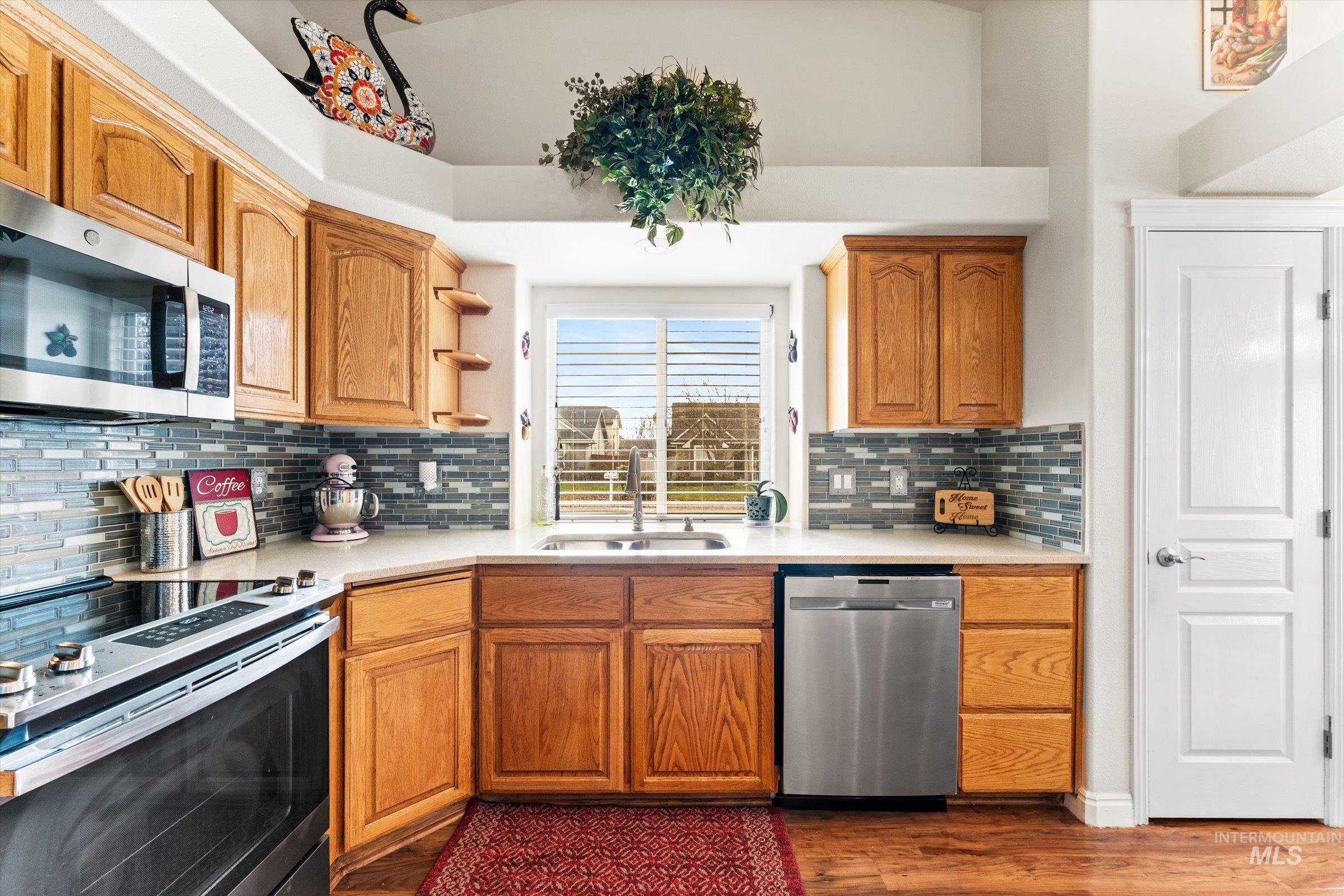 Kitchen with stainless steel appliances, light countertops, brown cabinetry, dark wood-type flooring, and open shelves
