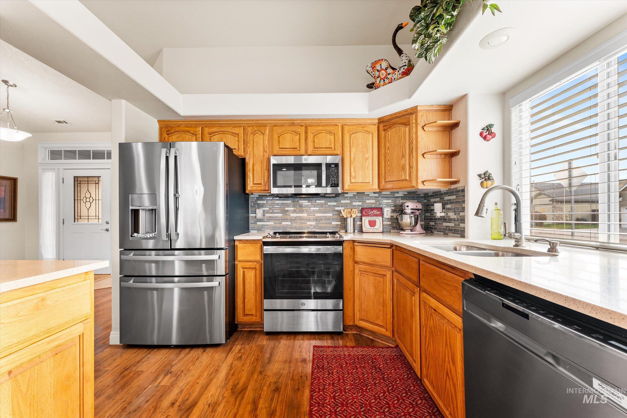 Kitchen with stainless steel appliances, light stone counters, open shelves, dark wood-style flooring, and pendant lighting