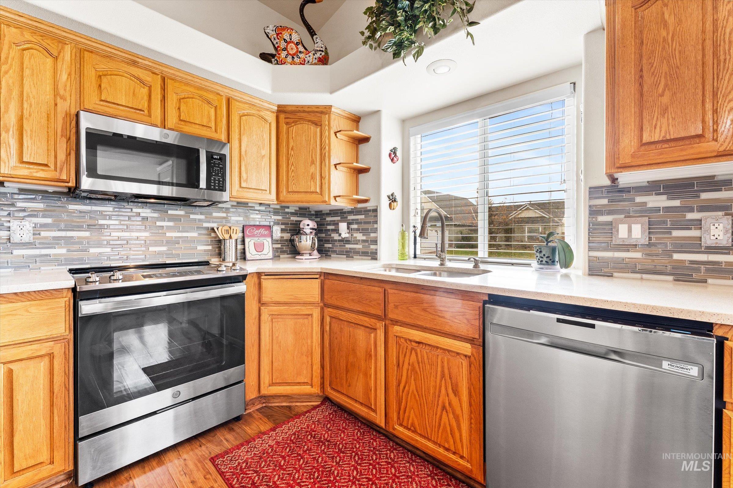 Kitchen with appliances with stainless steel finishes, light wood finished floors, open shelves, light stone countertops, and backsplash