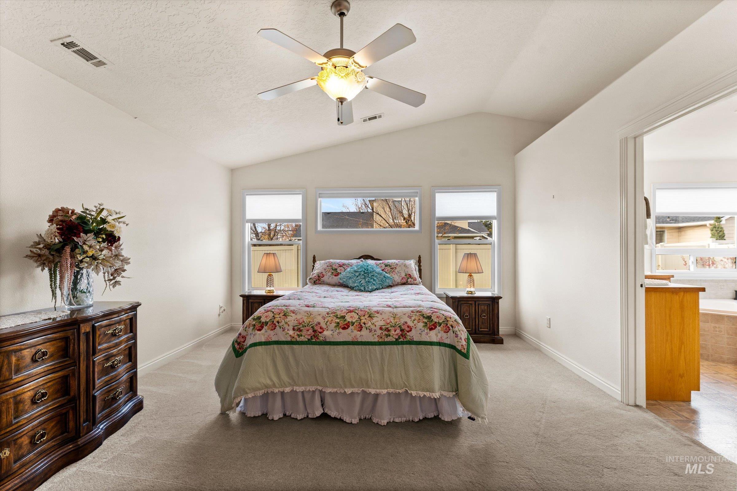 Bedroom with vaulted ceiling, ceiling fan, light colored carpet, and a textured ceiling