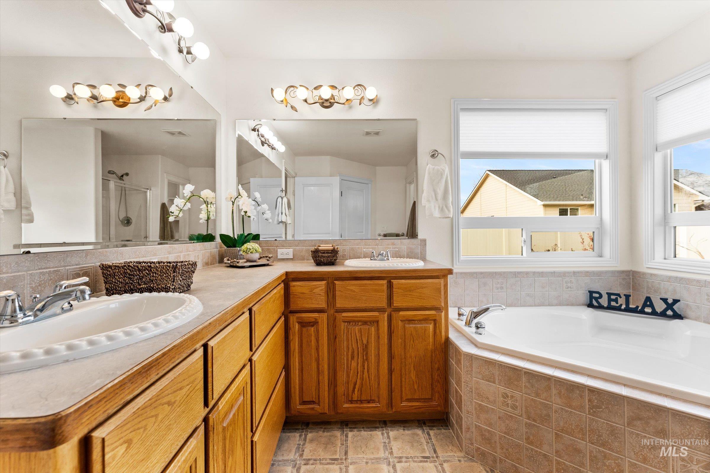 Full bathroom with double vanity, a stall shower, a garden tub, and stone tile floors