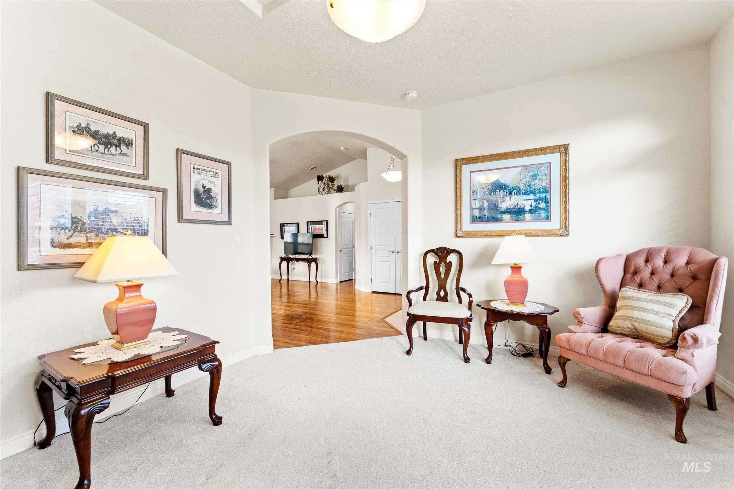 Sitting room featuring arched walkways, light colored carpet, and lofted ceiling