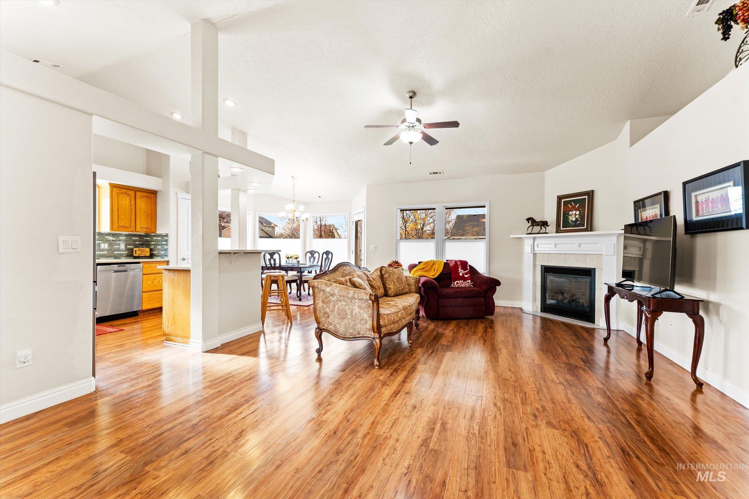 Living room with a fireplace, a ceiling fan, light wood finished floors, and a chandelier
