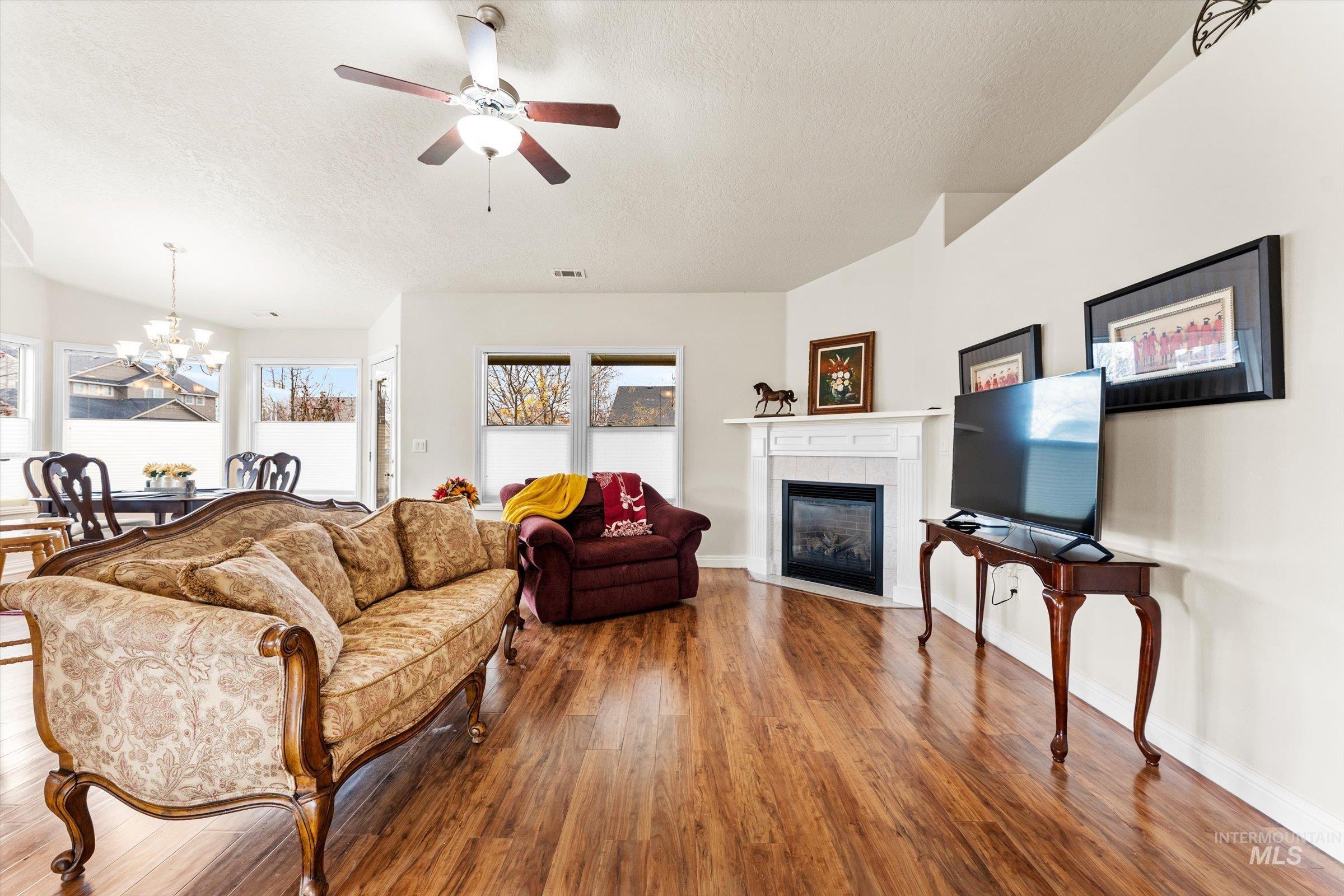 Living area featuring hardwood / wood-style floors, a chandelier, a textured ceiling, a tile fireplace, and a ceiling fan
