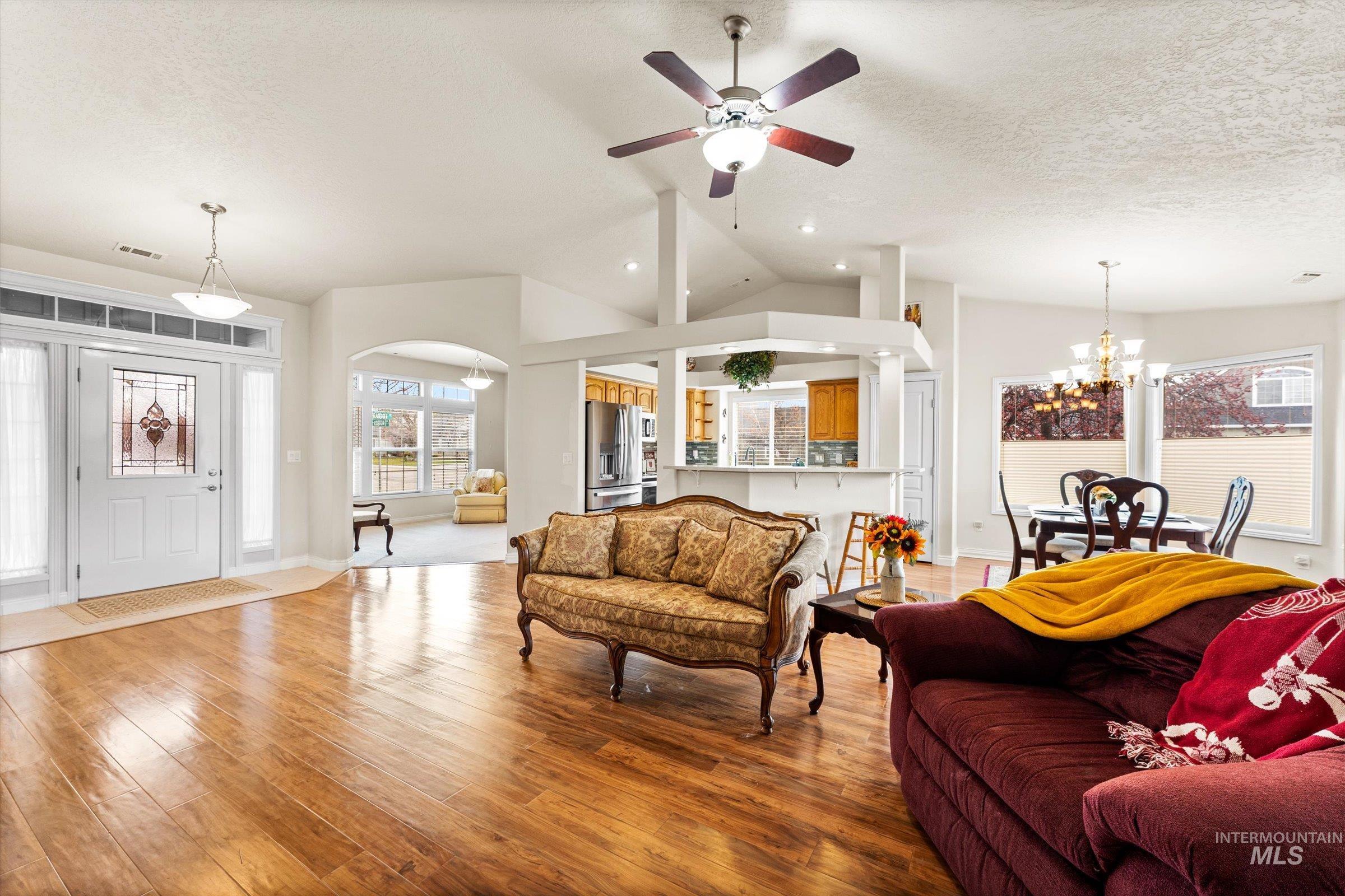 Living room featuring a chandelier, hardwood / wood-style flooring, a ceiling fan, vaulted ceiling, and a textured ceiling
