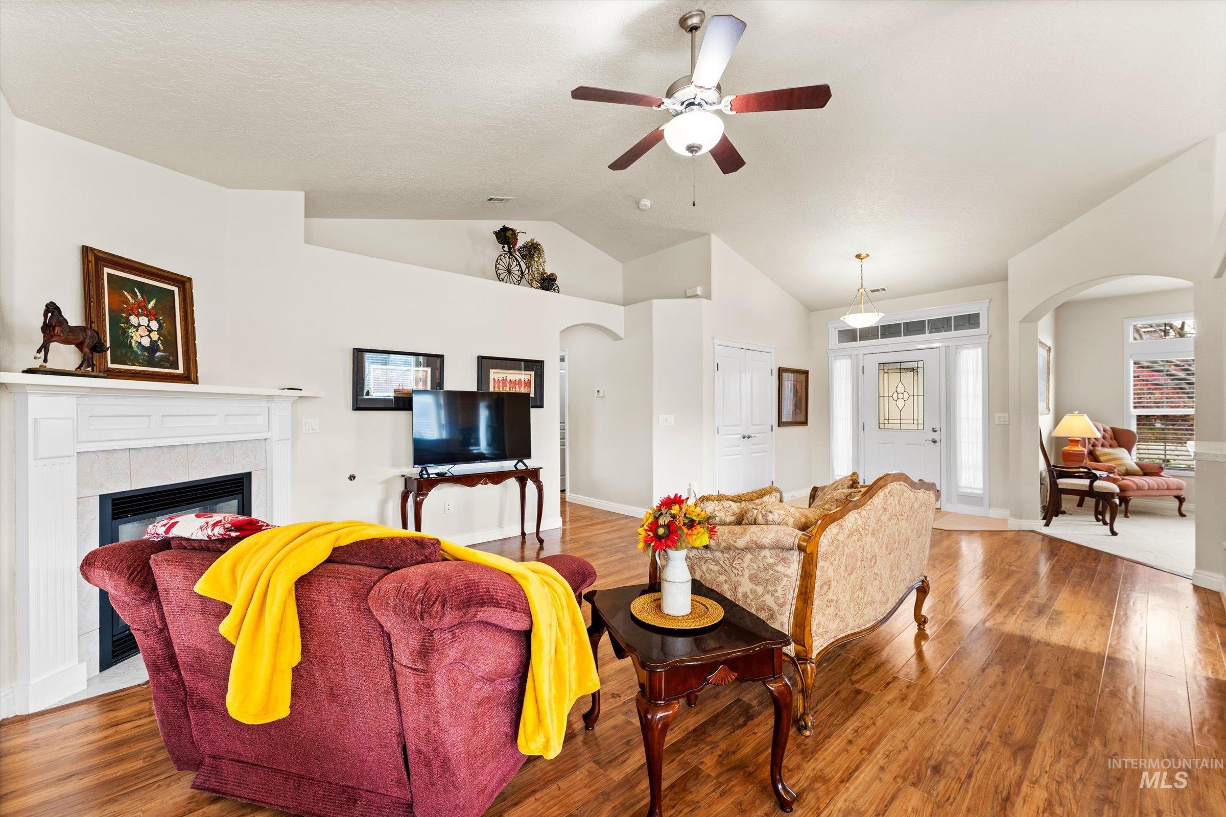 Living area with arched walkways, lofted ceiling, wood finished floors, a ceiling fan, and a fireplace