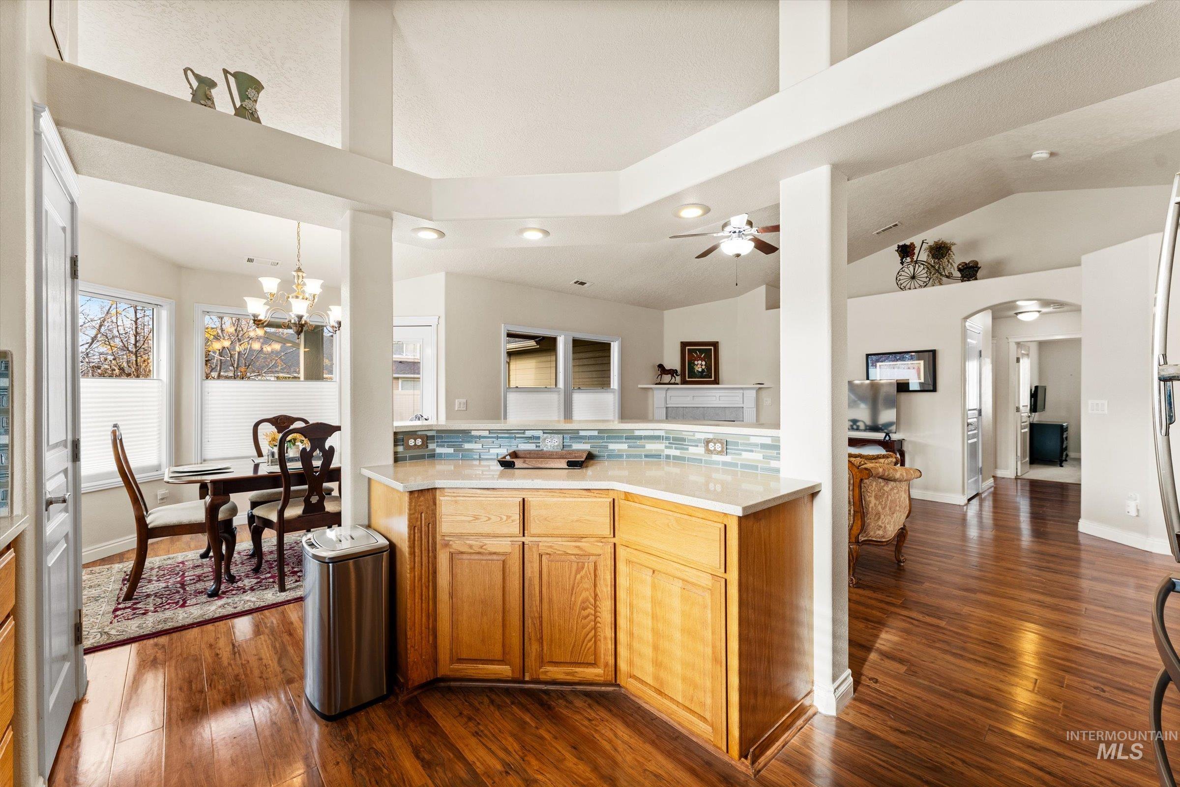 Kitchen with dark wood finished floors, arched walkways, backsplash, brown cabinets, and high vaulted ceiling