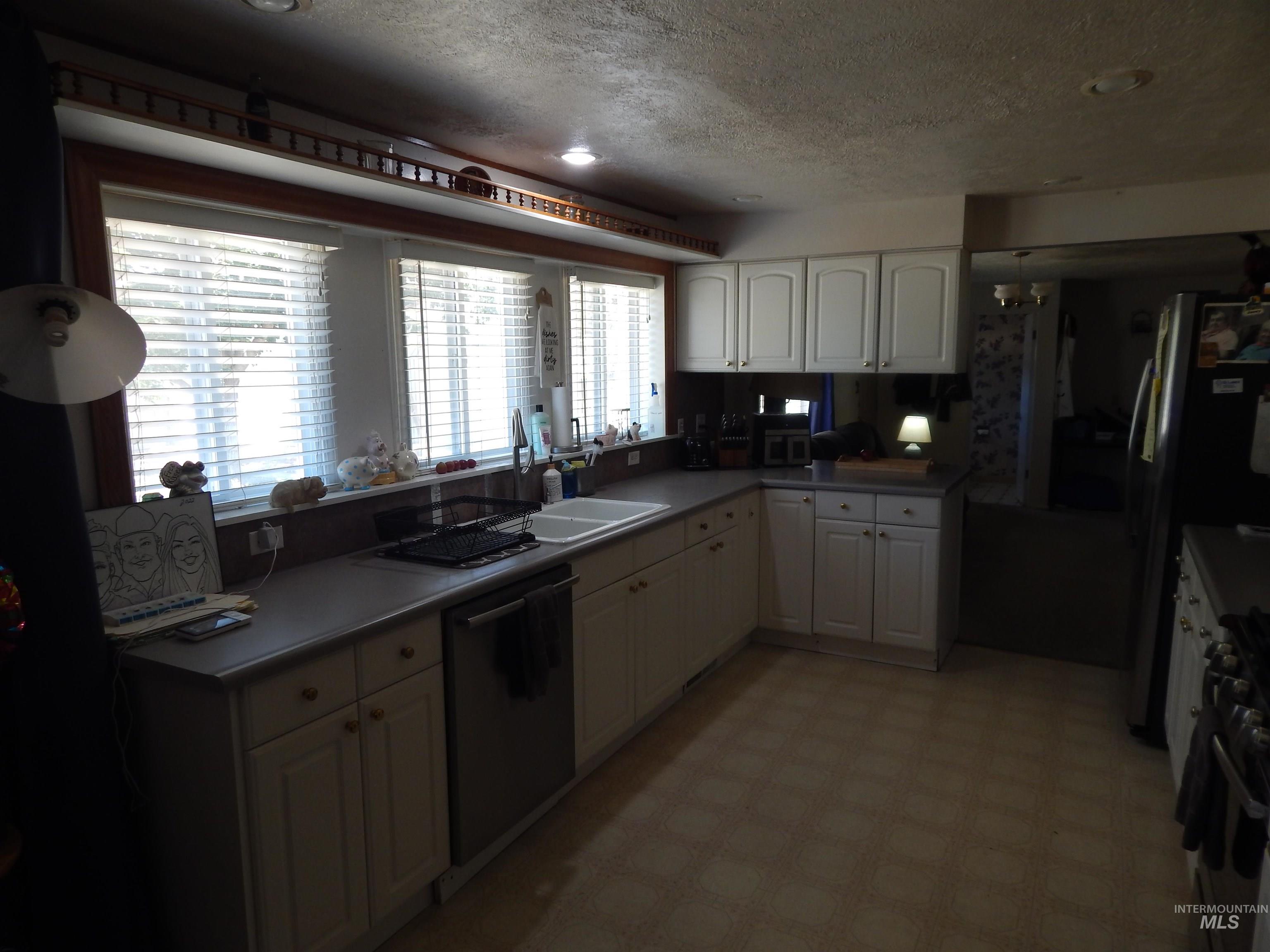 Kitchen featuring light flooring, stainless steel appliances, a textured ceiling, white cabinets, and light countertops