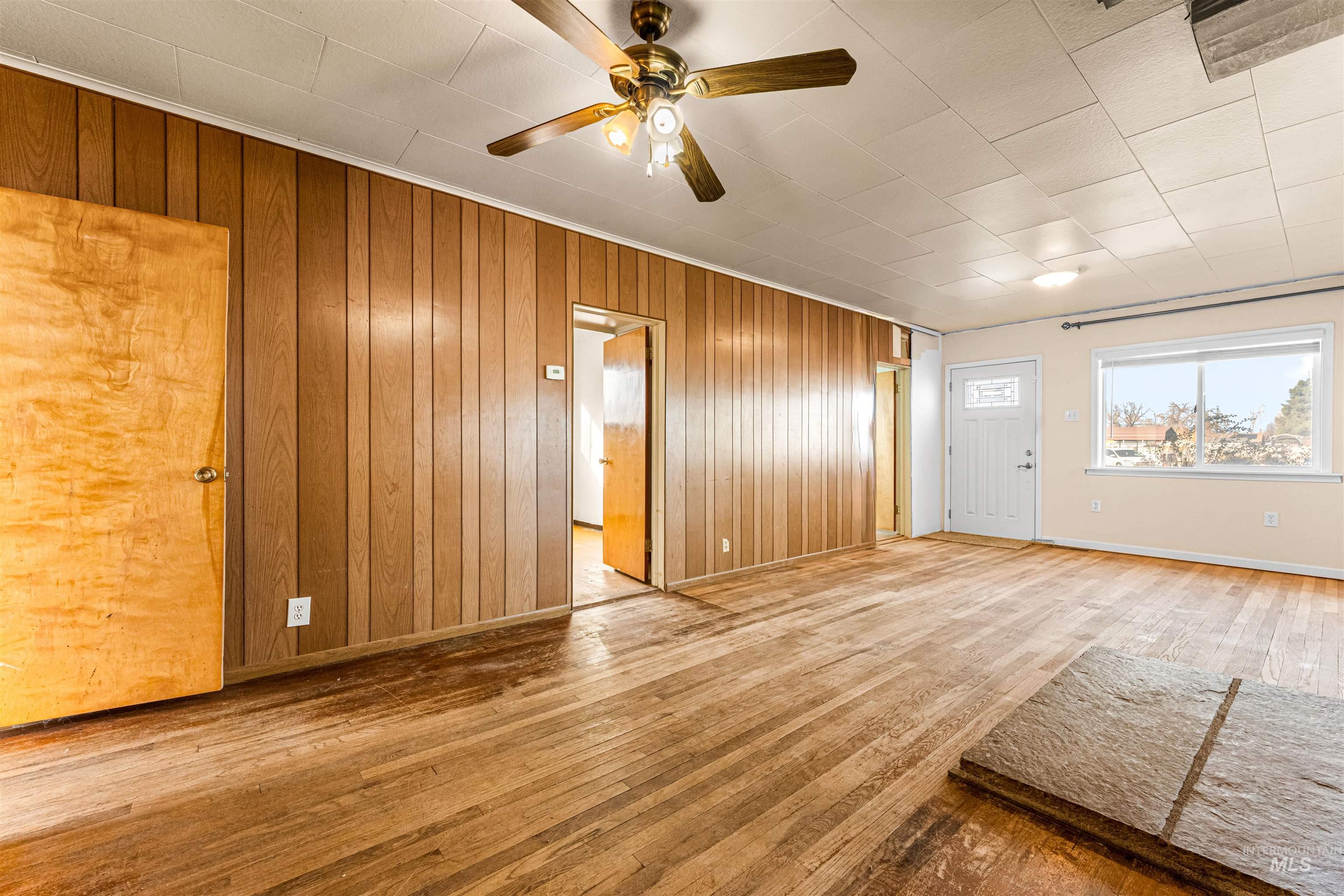 Unfurnished living room featuring hardwood / wood-style flooring, wooden walls, and a ceiling fan
