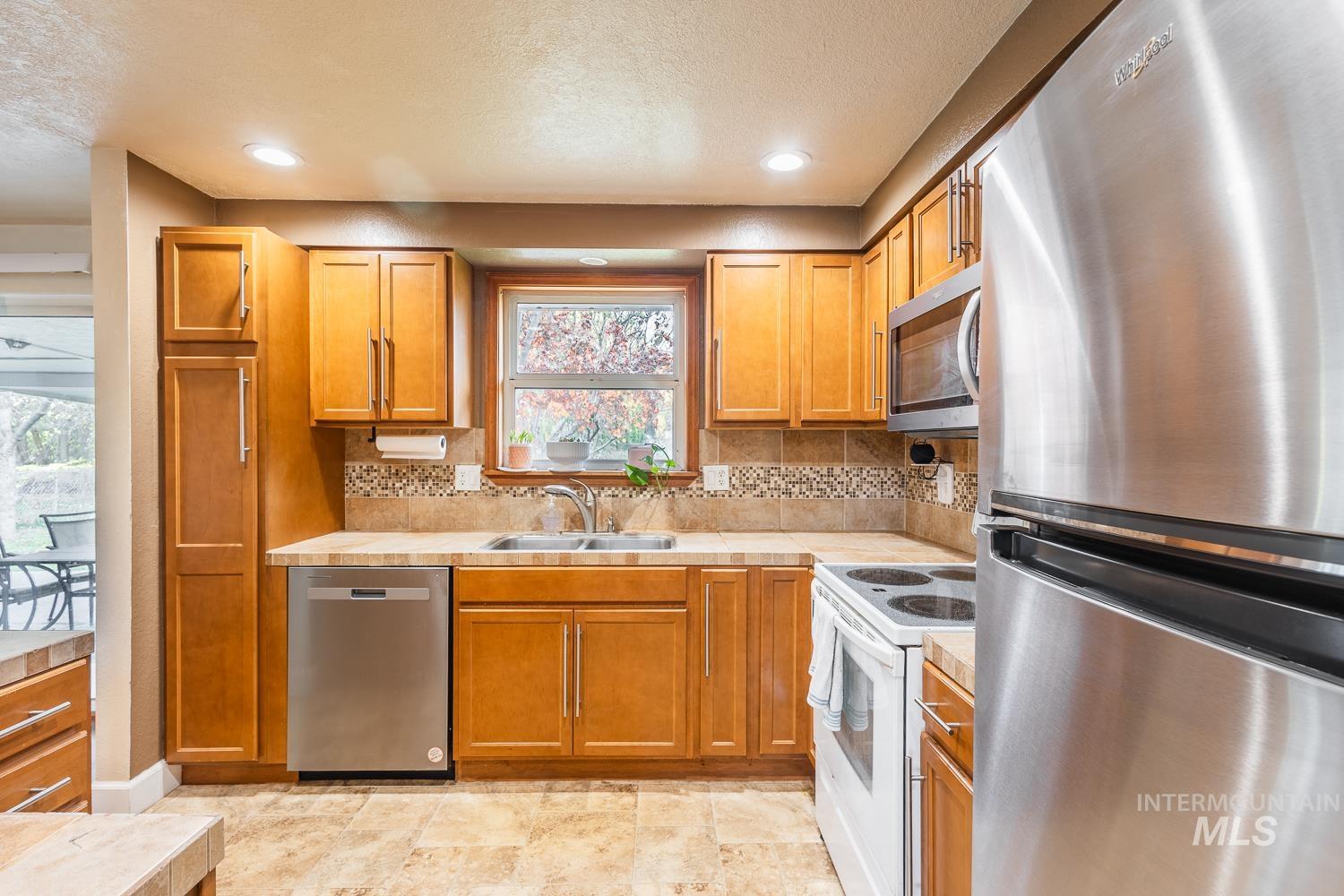 Kitchen featuring stainless steel appliances, backsplash, brown cabinetry, a textured ceiling, and recessed lighting