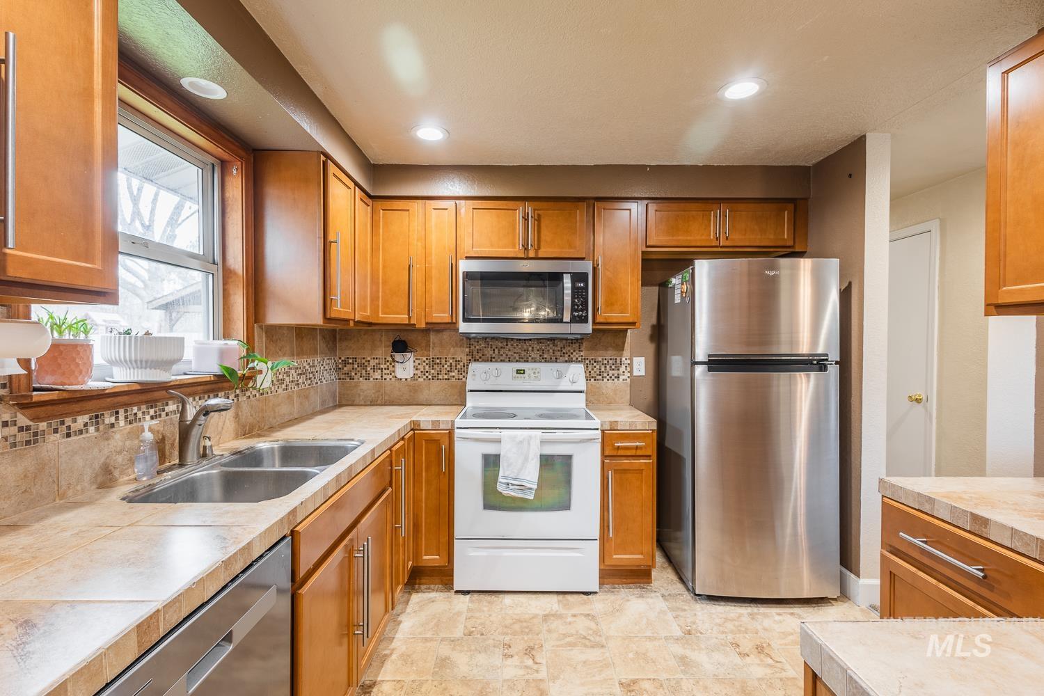 Kitchen featuring appliances with stainless steel finishes, brown cabinets, backsplash, recessed lighting, and tile counters