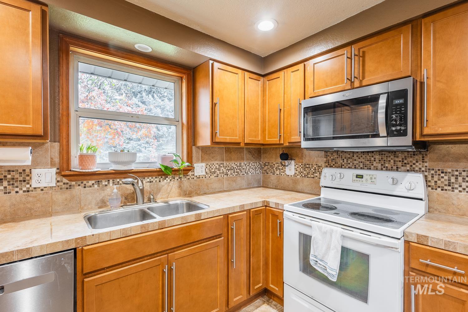 Kitchen featuring appliances with stainless steel finishes, brown cabinets, decorative backsplash, and recessed lighting
