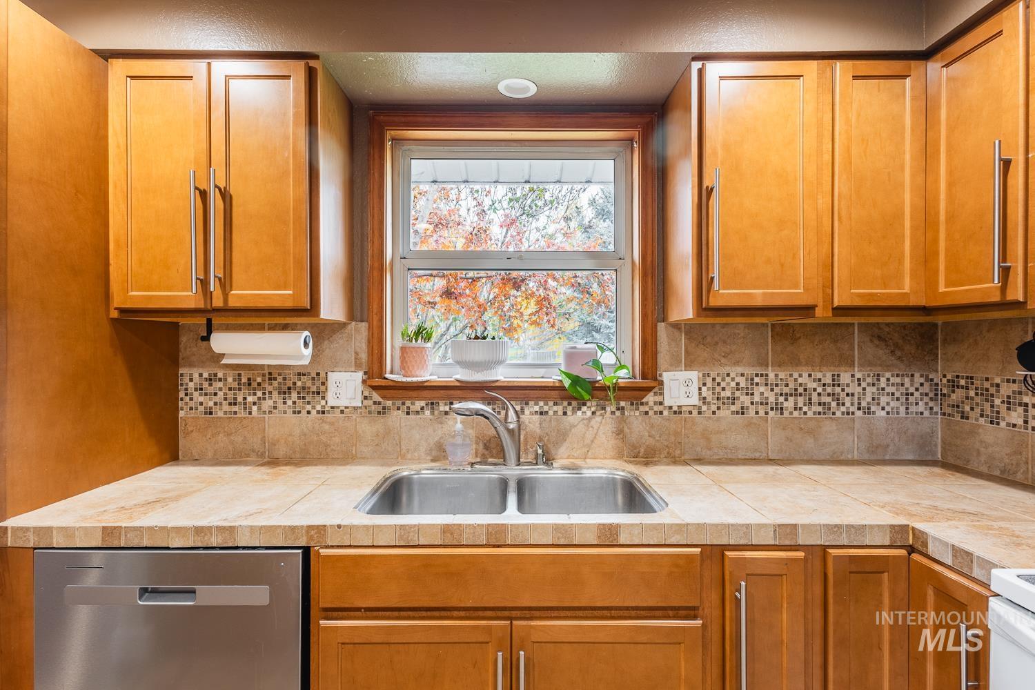 Kitchen featuring brown cabinetry, light countertops, dishwasher, white range, and decorative backsplash