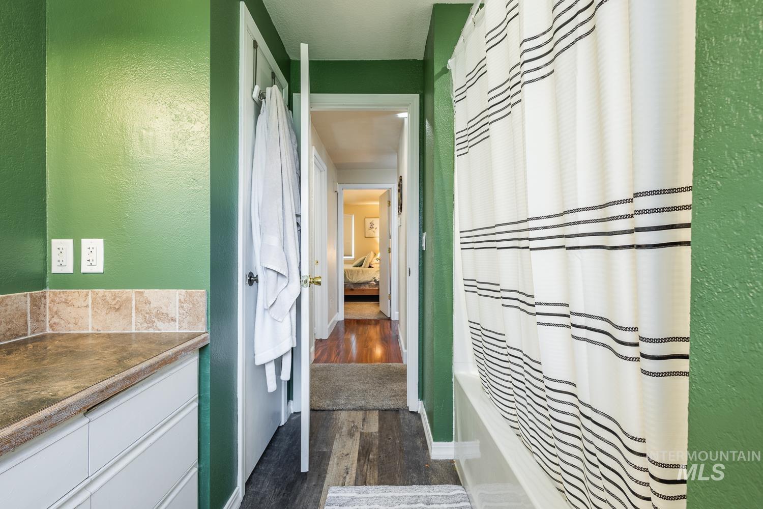 Bathroom featuring a textured wall, shower / bath combo, dark wood-style flooring, ensuite bath, and vanity