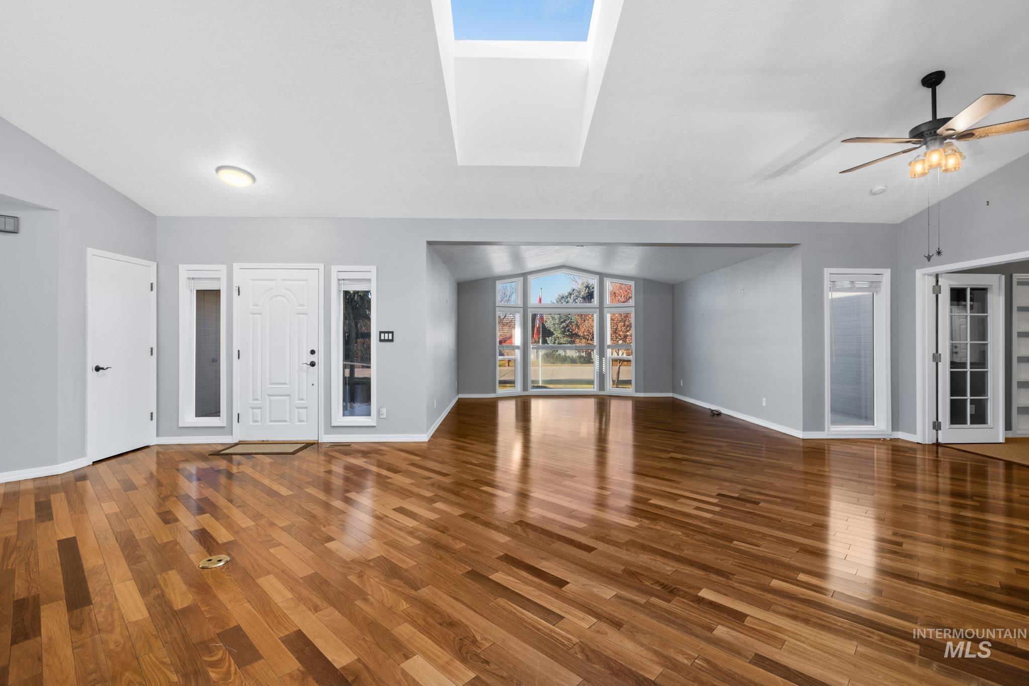 Unfurnished living room featuring a skylight, lofted ceiling, and wood finished floors