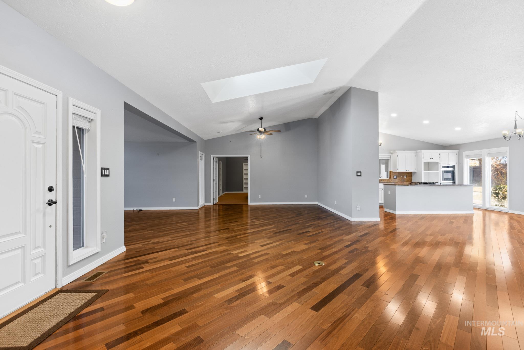 Unfurnished living room featuring a skylight, a ceiling fan, dark wood-style floors, vaulted ceiling, and recessed lighting