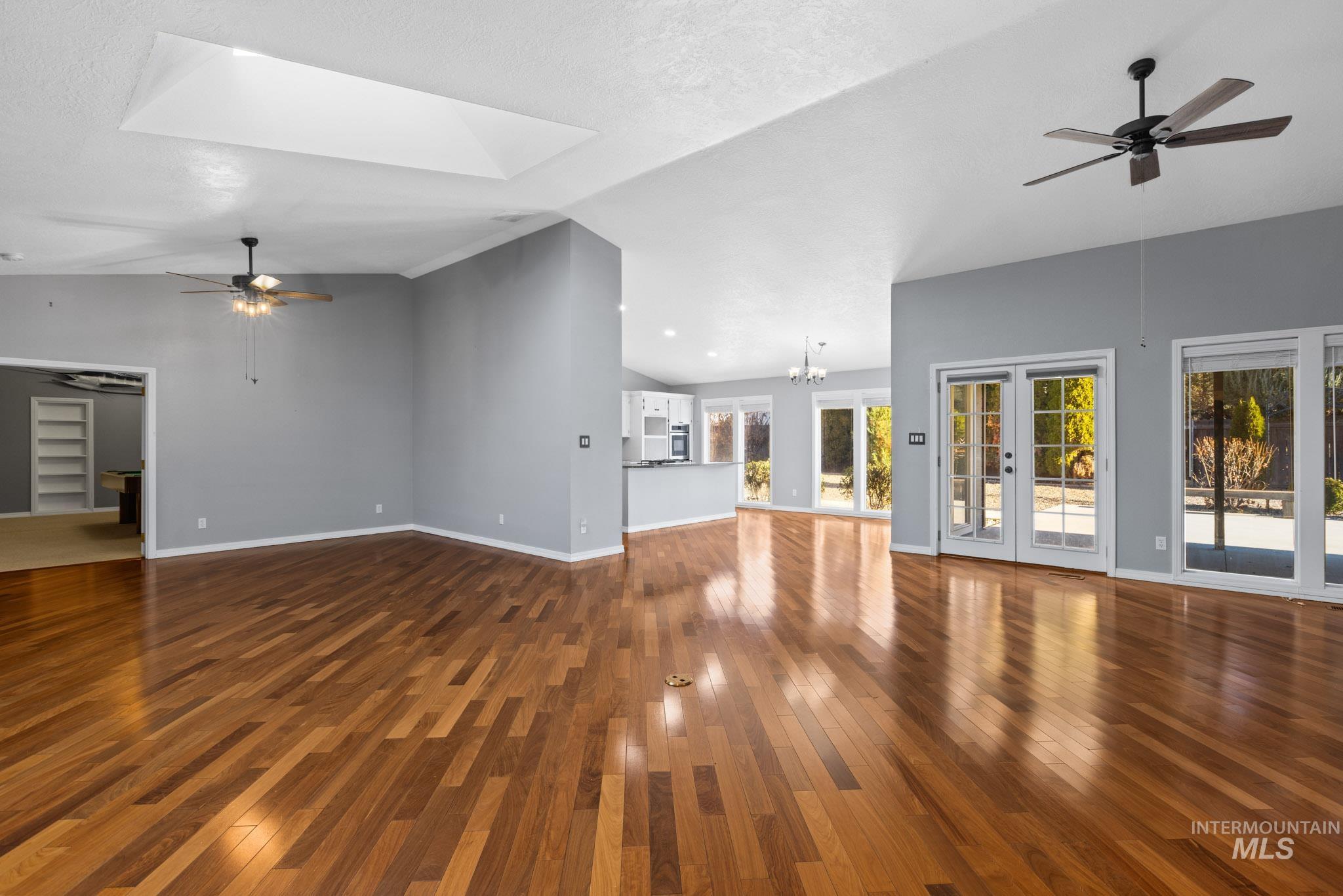 Unfurnished living room featuring ceiling fan, a chandelier, lofted ceiling, dark wood-style floors, and a skylight