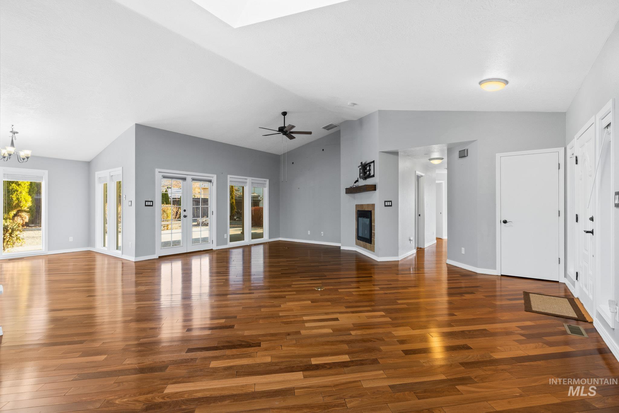 Unfurnished living room featuring a tile fireplace, dark wood-style floors, lofted ceiling, a skylight, and a chandelier