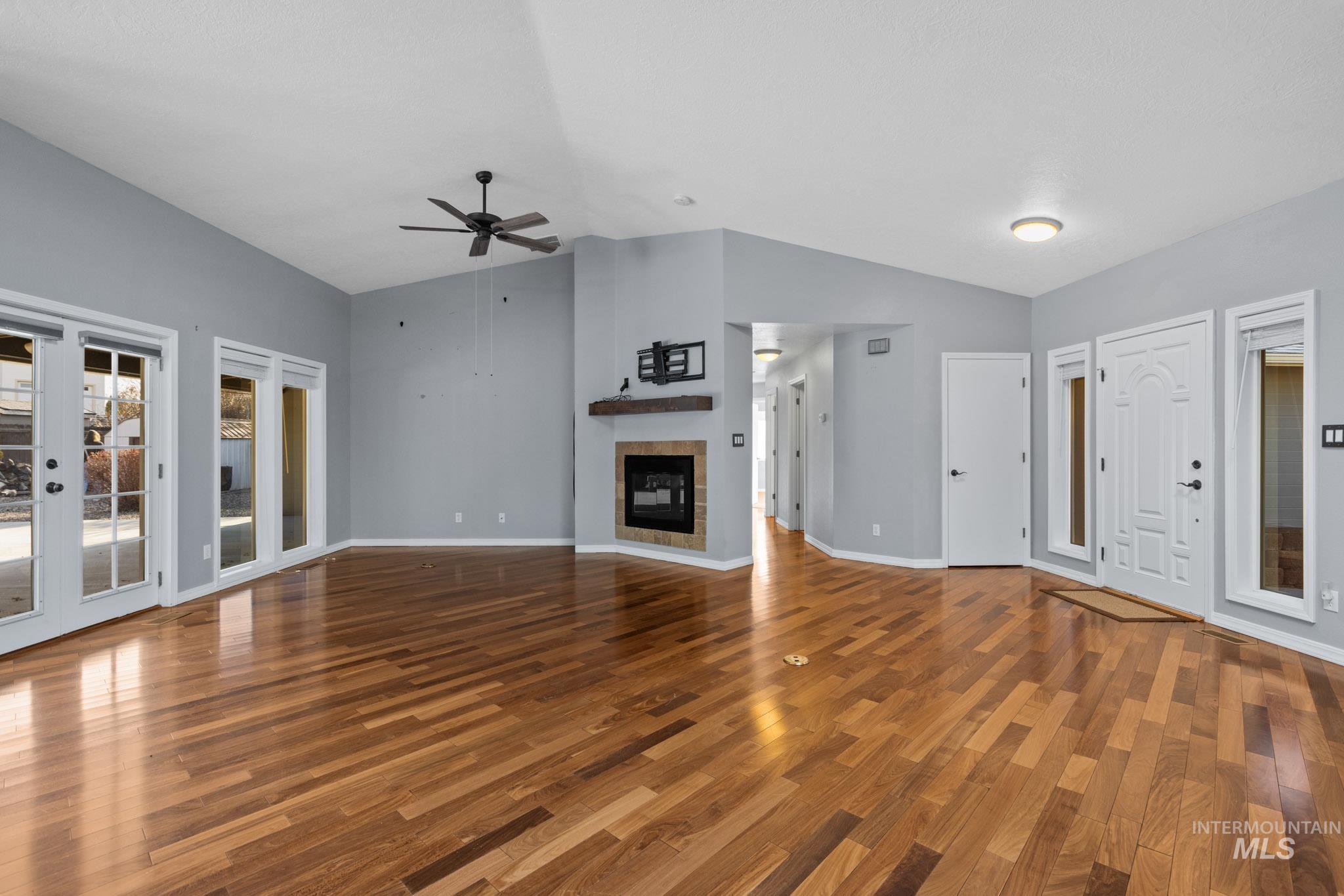 Unfurnished living room featuring a tiled fireplace, wood finished floors, vaulted ceiling, and ceiling fan