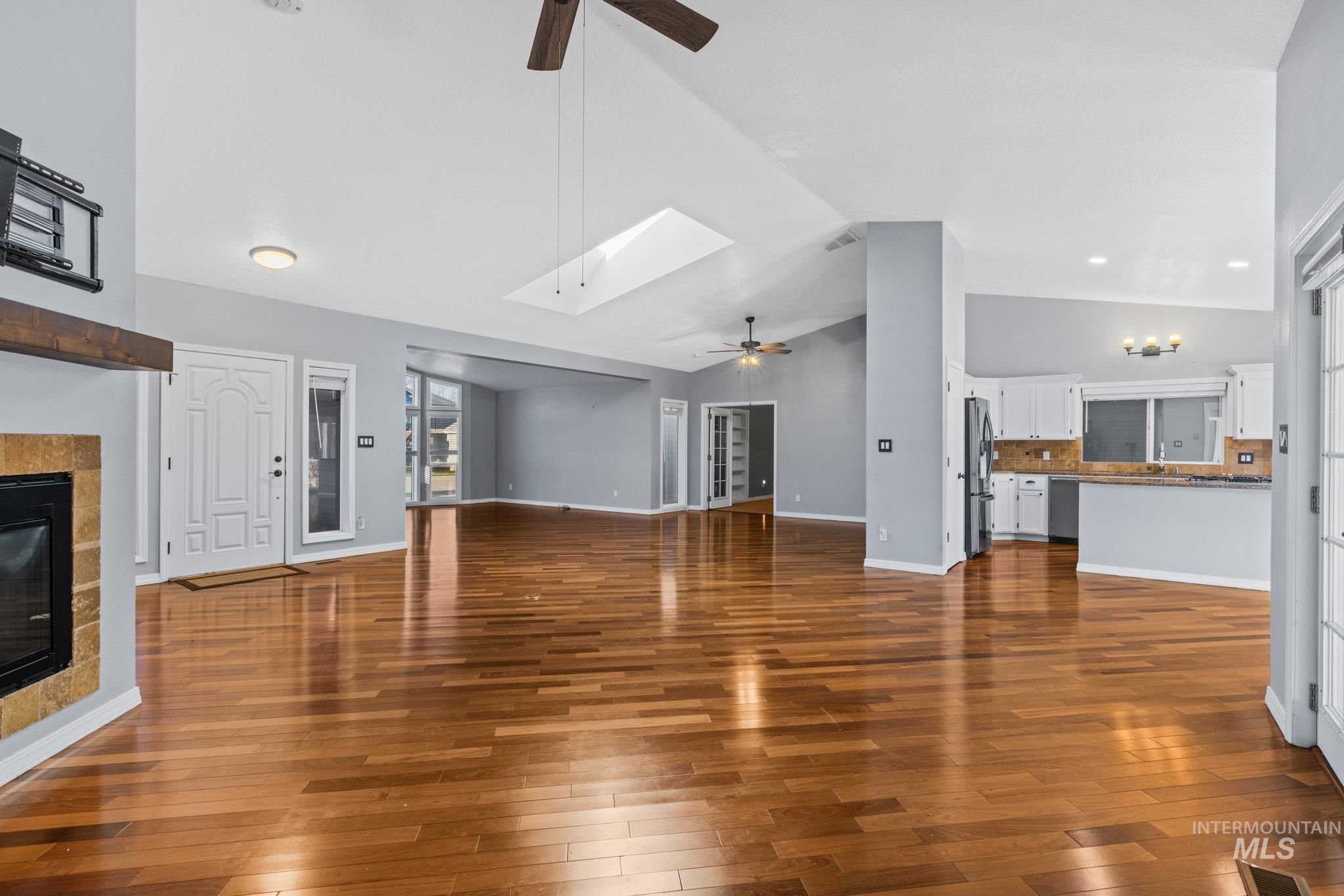 Unfurnished living room with a ceiling fan, a tiled fireplace, dark wood-style flooring, a skylight, and high vaulted ceiling