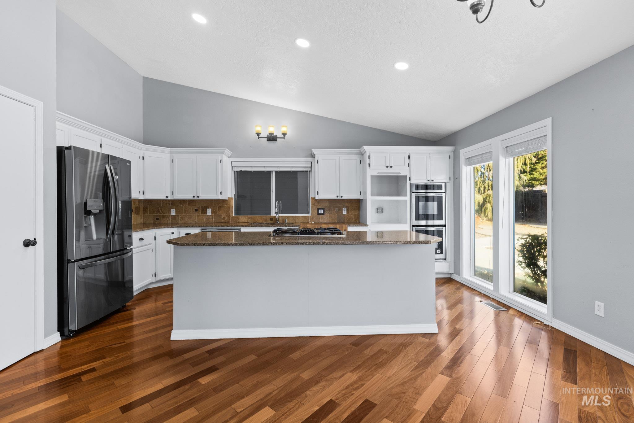 Kitchen with tasteful backsplash, dark stone counters, a kitchen island, white cabinets, and stainless steel appliances