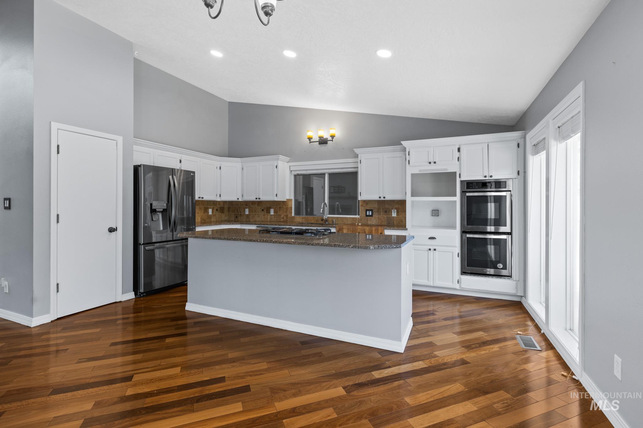 Kitchen featuring white cabinets, a kitchen island, backsplash, stainless steel appliances, and dark stone countertops