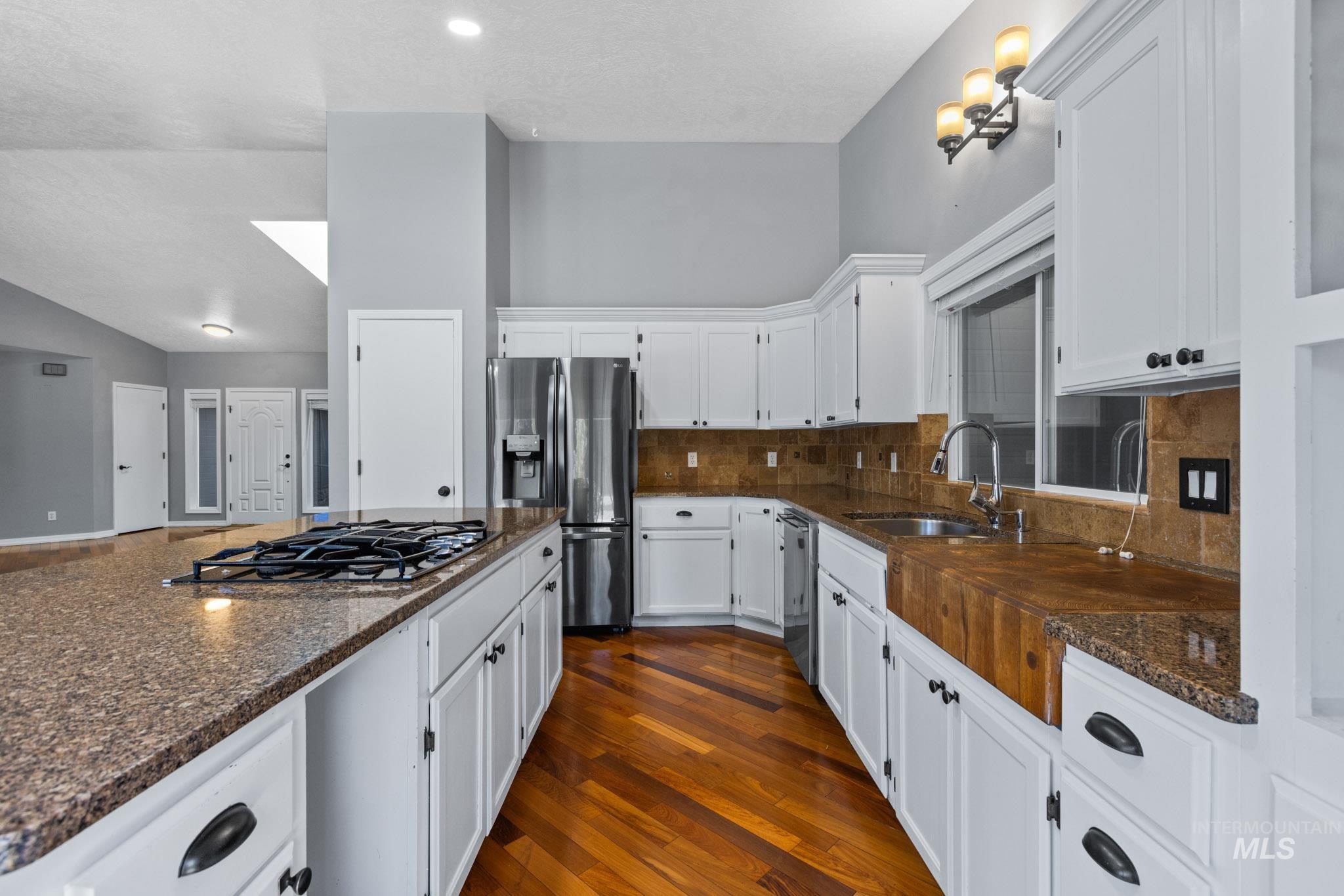 Kitchen featuring white cabinetry, dark wood-type flooring, appliances with stainless steel finishes, dark stone countertops, and lofted ceiling