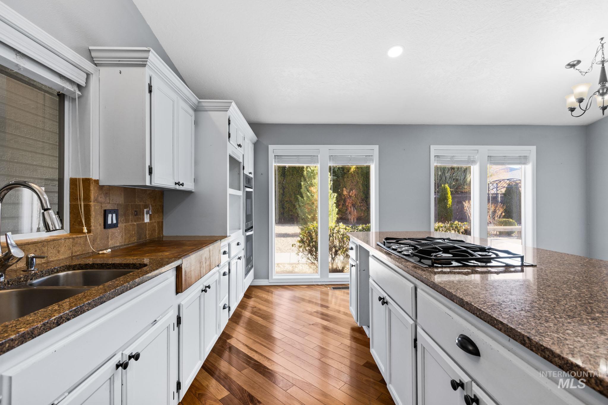 Kitchen featuring white cabinetry, dark stone countertops, decorative backsplash, dark wood-style flooring, and black gas stovetop