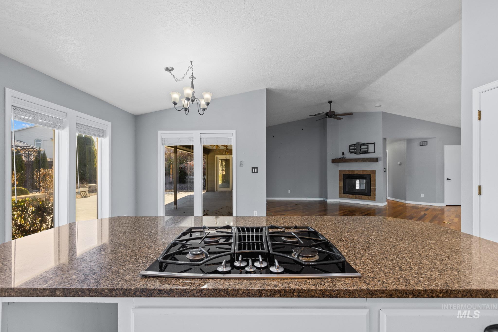 Kitchen featuring lofted ceiling, a tiled fireplace, black gas stovetop, a chandelier, and a center island