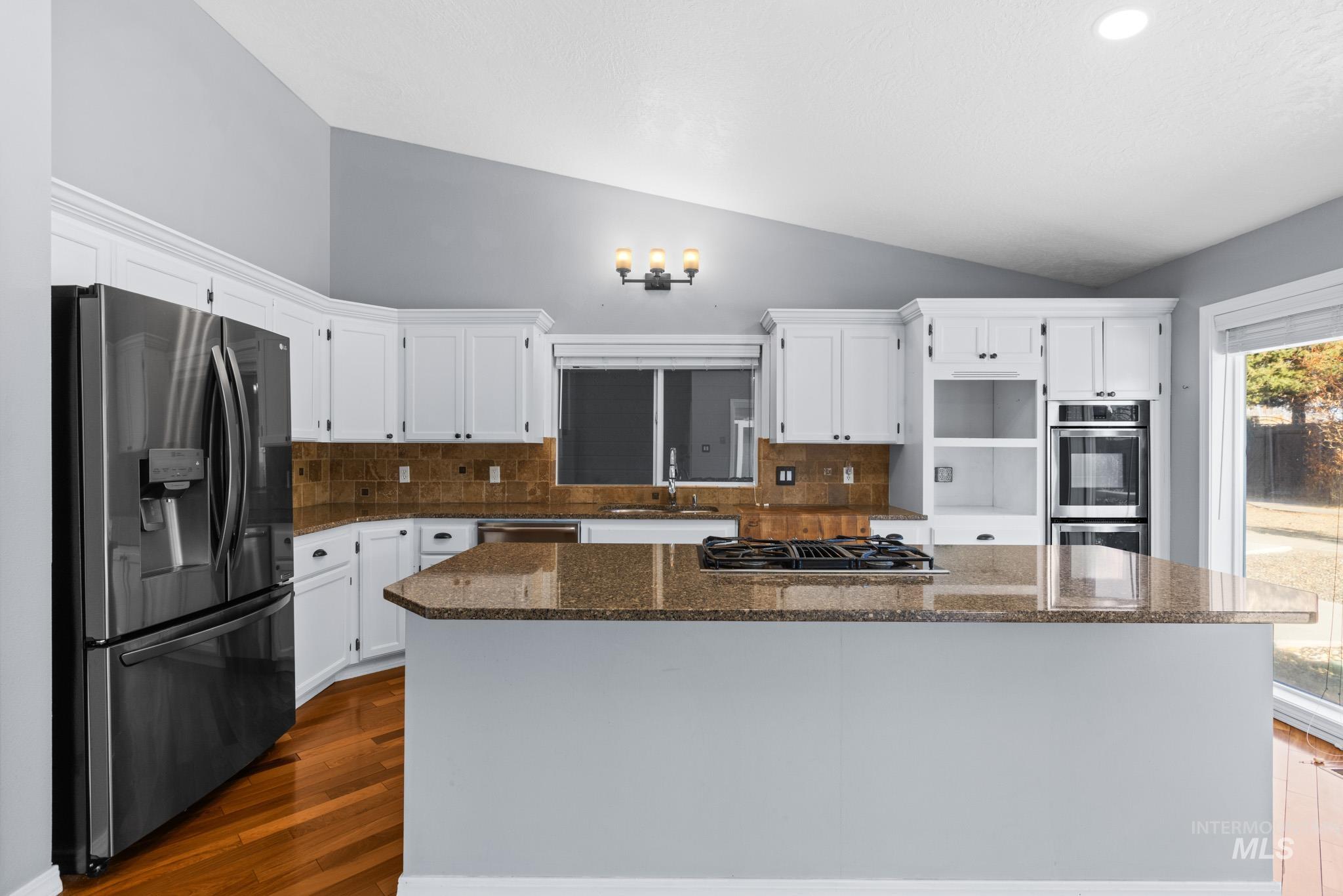 Kitchen with decorative backsplash, stainless steel appliances, a center island, white cabinets, and lofted ceiling
