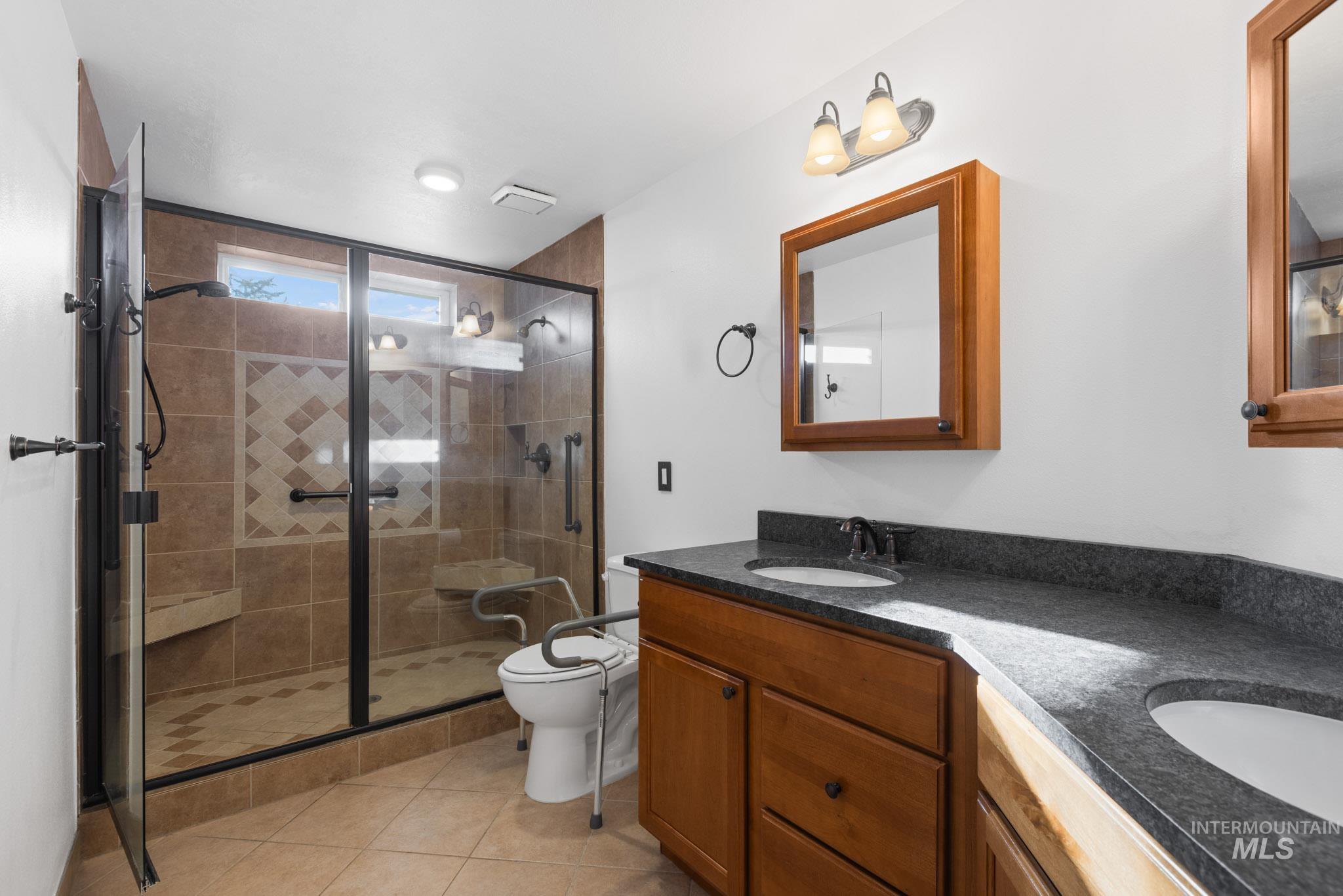 Full bathroom featuring double vanity, a shower stall, and light tile patterned floors