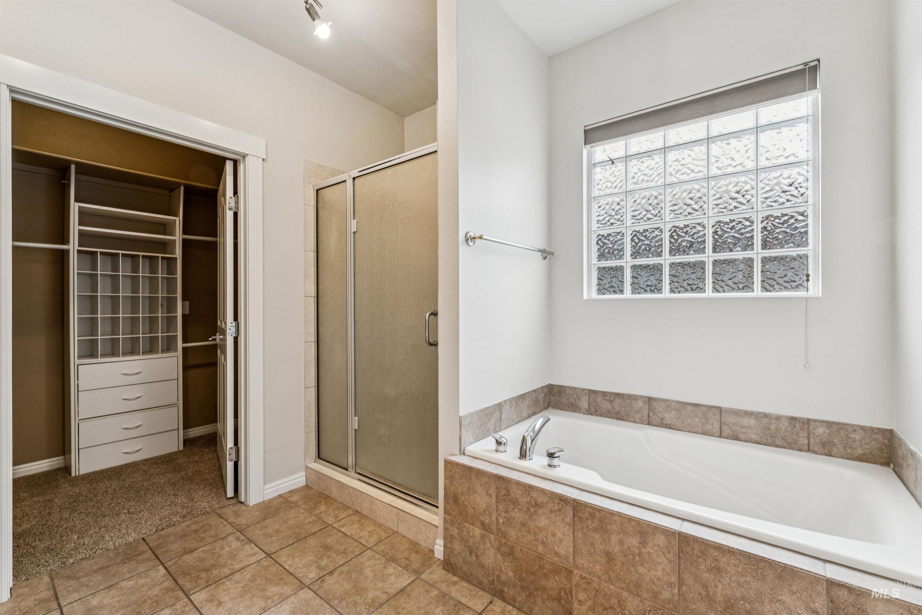Bathroom with a walk in closet, a shower stall, a garden tub, and tile patterned flooring