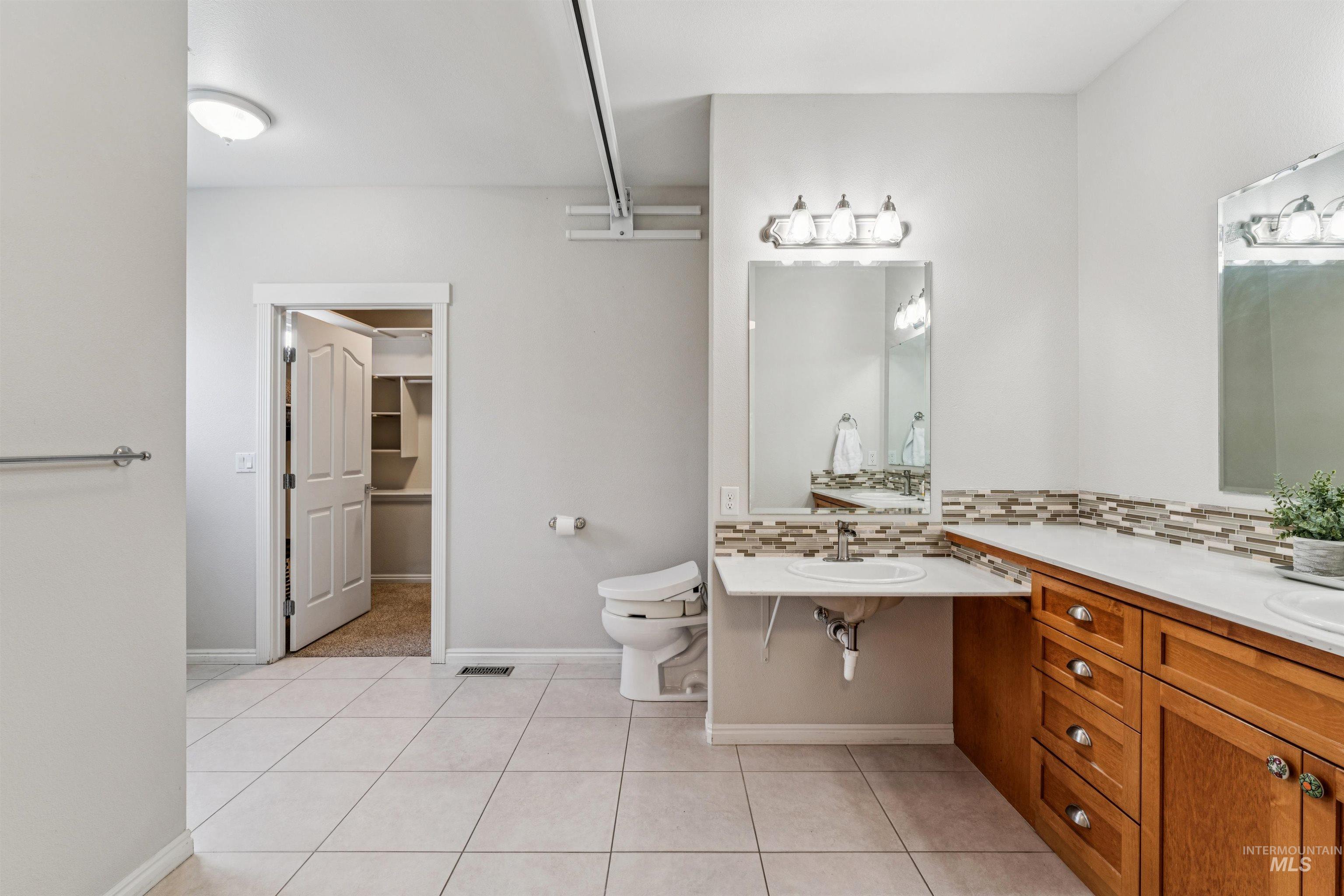 Full bath featuring vanity, light tile patterned floors, tasteful backsplash, and a walk in closet