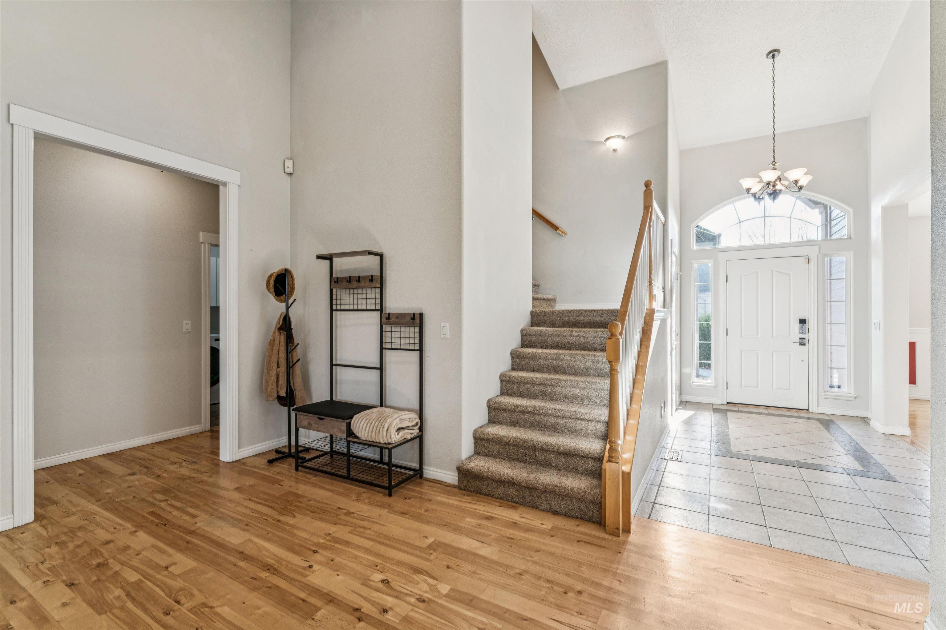Entryway featuring a towering ceiling, light wood-type flooring, stairs, and a chandelier