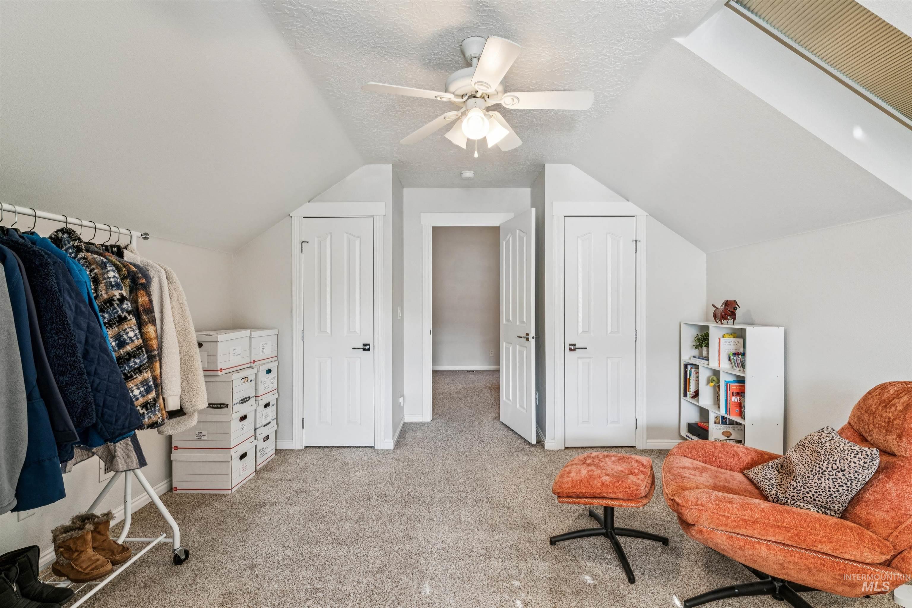 Living area with vaulted ceiling, light colored carpet, ceiling fan, and a textured ceiling