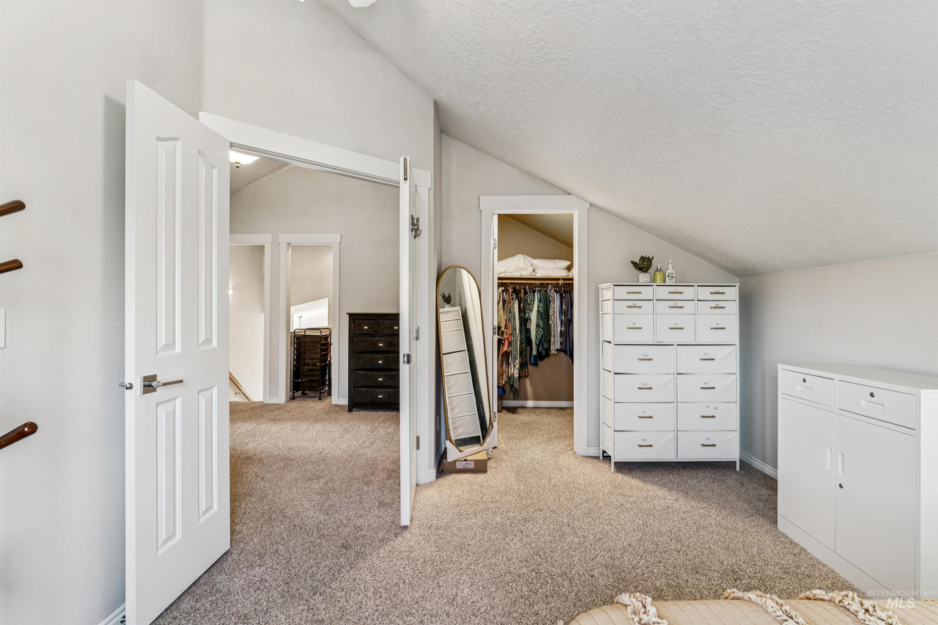 Unfurnished bedroom featuring lofted ceiling, a spacious closet, a textured ceiling, and light colored carpet