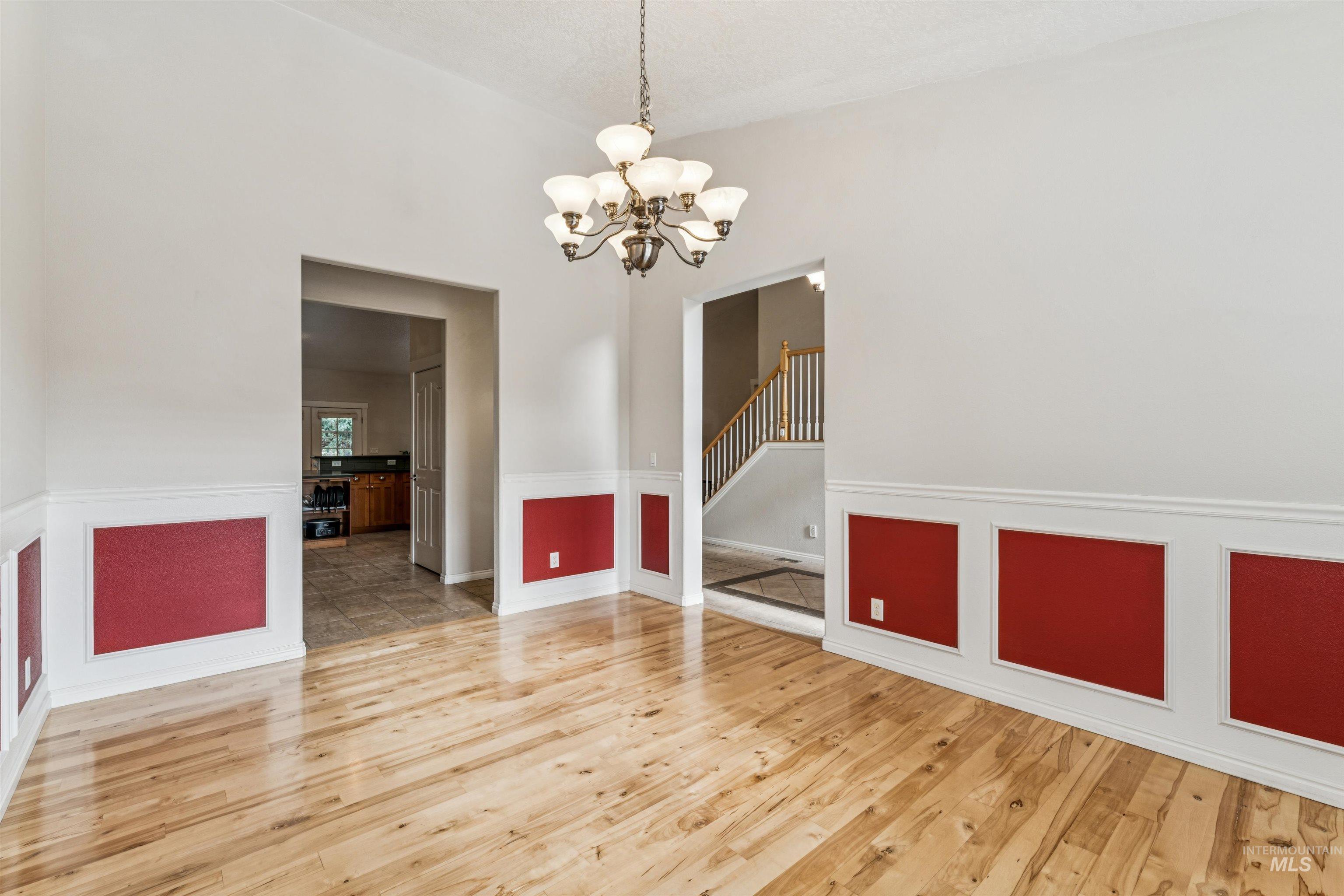 Unfurnished room with a chandelier, light wood-style floors, a wainscoted wall, and stairway